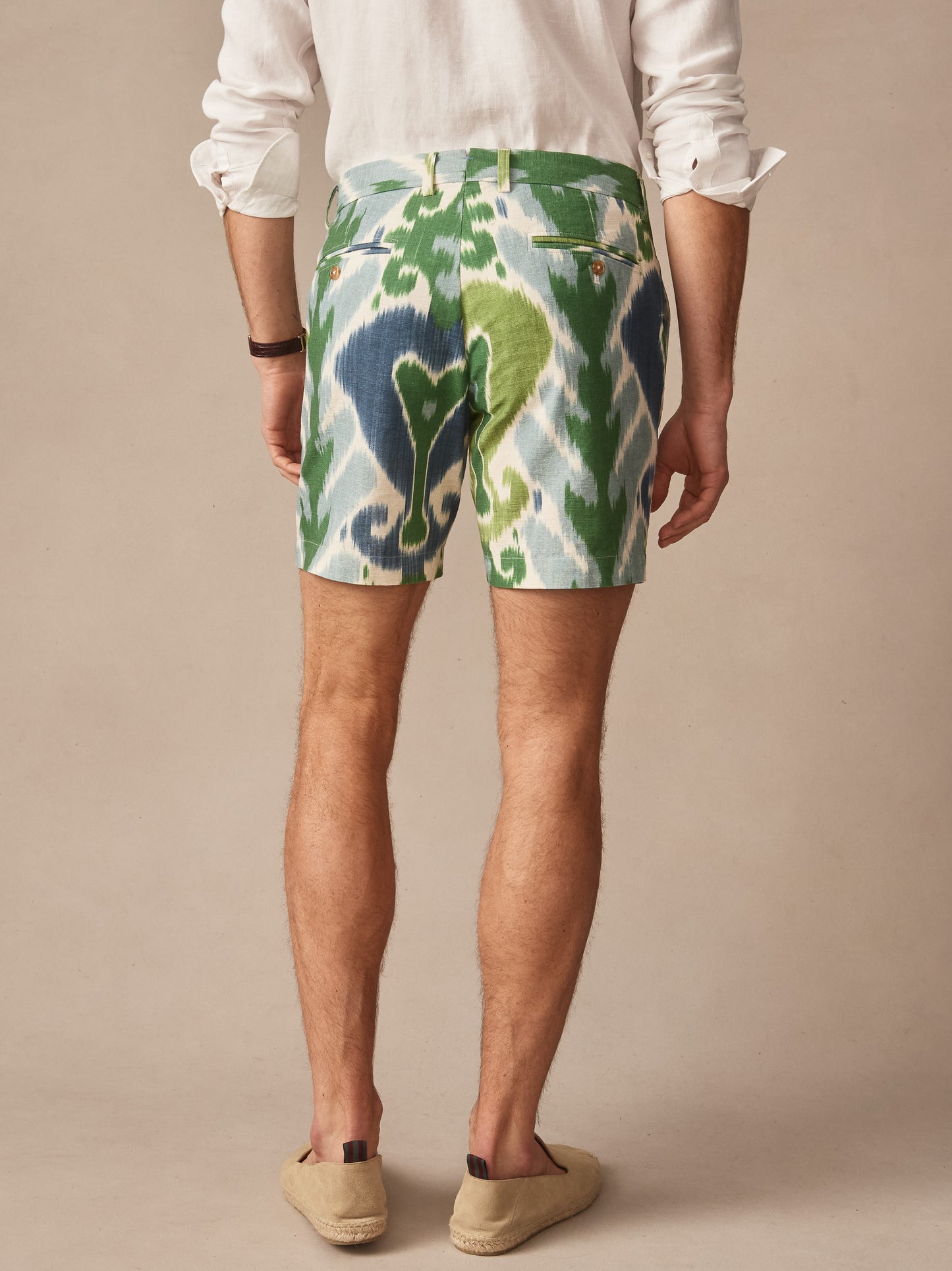 Rear view of a man wearing J.McLaughlin Chatham Shorts in Ikat featuring a blue and green patterned design, paired with a white shirt and casual slip-on shoes, showcasing effortlessly stylish, enduring designs with innovative fabrics. A destination for defining style. Life, Well-Lived.