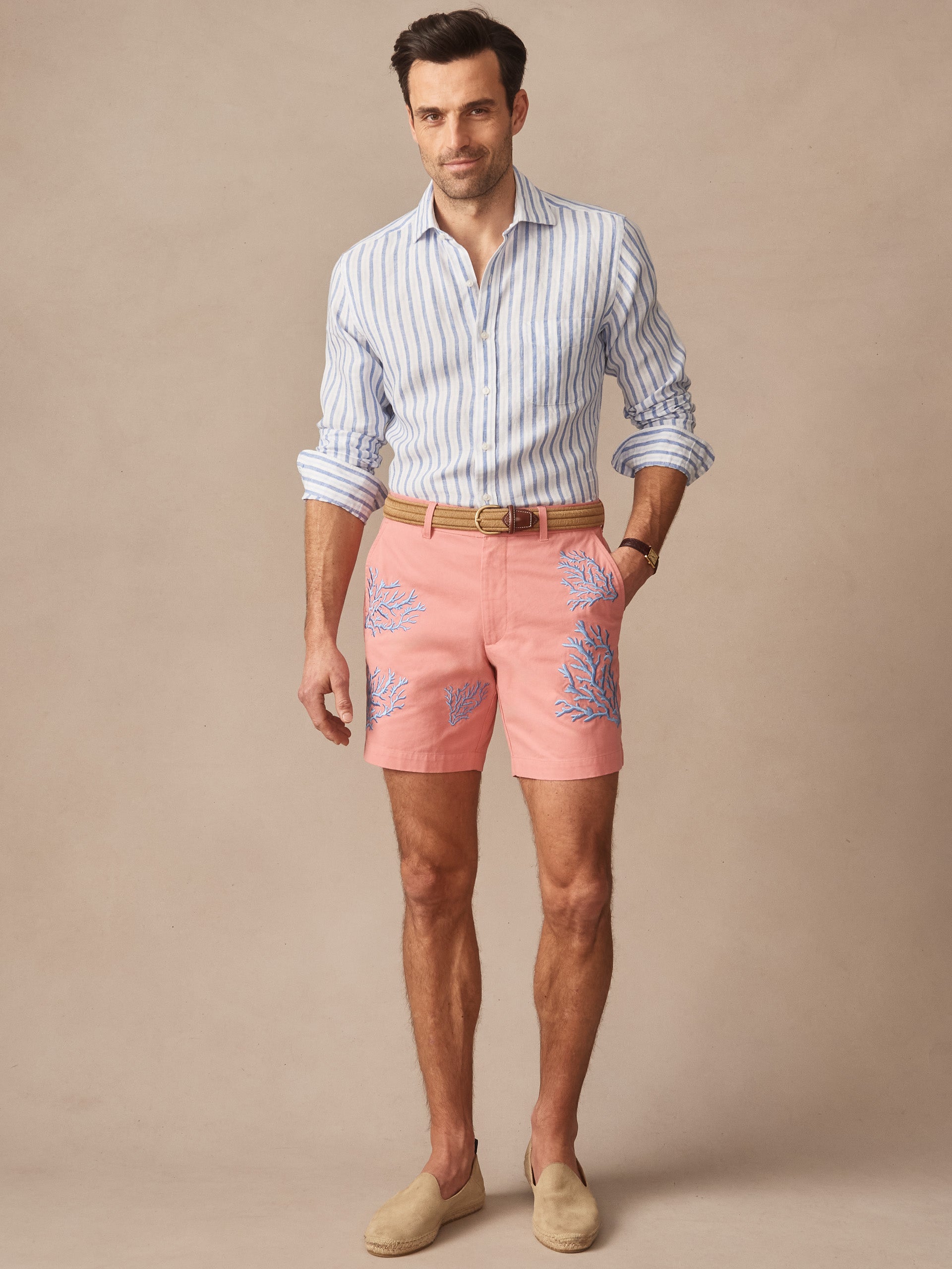 Man wearing a striped long-sleeve shirt paired with Chatham Embroidered Shorts in Coral by J.McLaughlin, showcasing effortlessly stylish shorts with enduring designs in innovative fabrics.