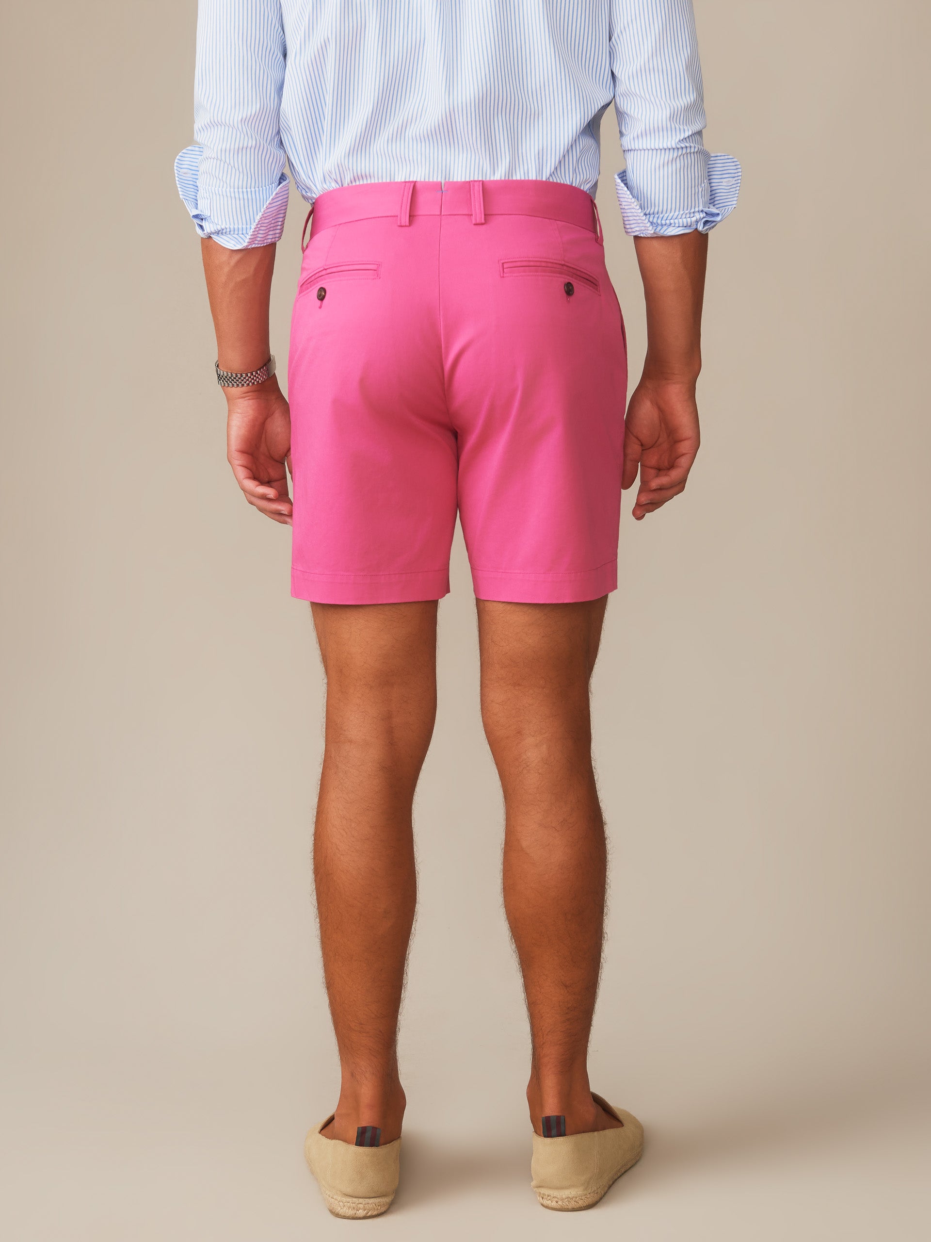 Man wearing bright pink Chatham Shorts by J.McLaughlin, paired with a light blue striped shirt, showcasing effortlessly stylish, enduring designs in innovative fabrics for a life well-lived.