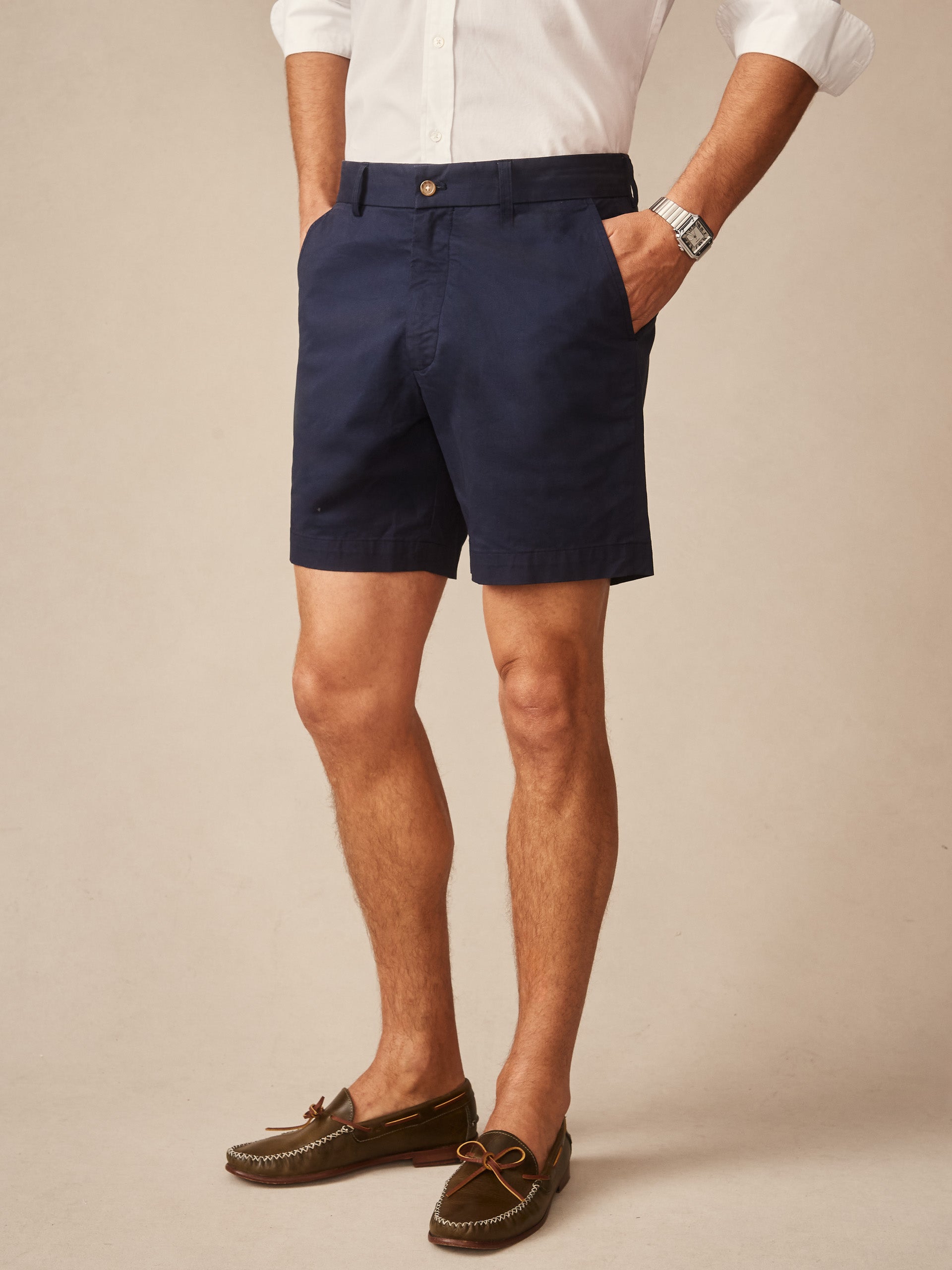 A man wearing navy Chatham Shorts by J.McLaughlin paired with a white shirt and brown loafers, showcasing effortlessly stylish, enduring designs with a legacy of timeless fashion.