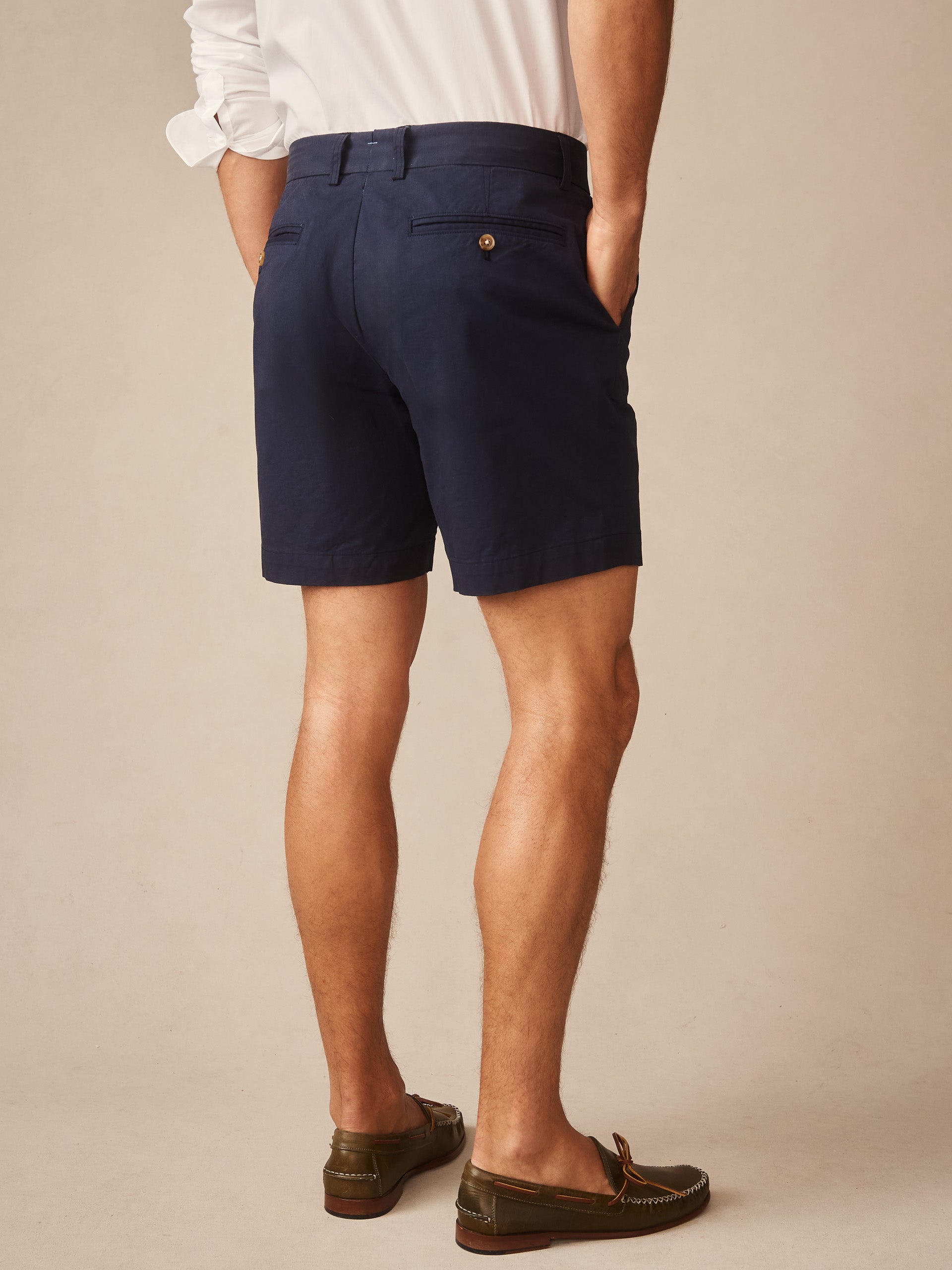 Man wearing navy blue Chatham Shorts by J.McLaughlin, paired with a white shirt and brown loafers, showcasing effortlessly stylish, enduring designs and a legacy of timeless fashion.