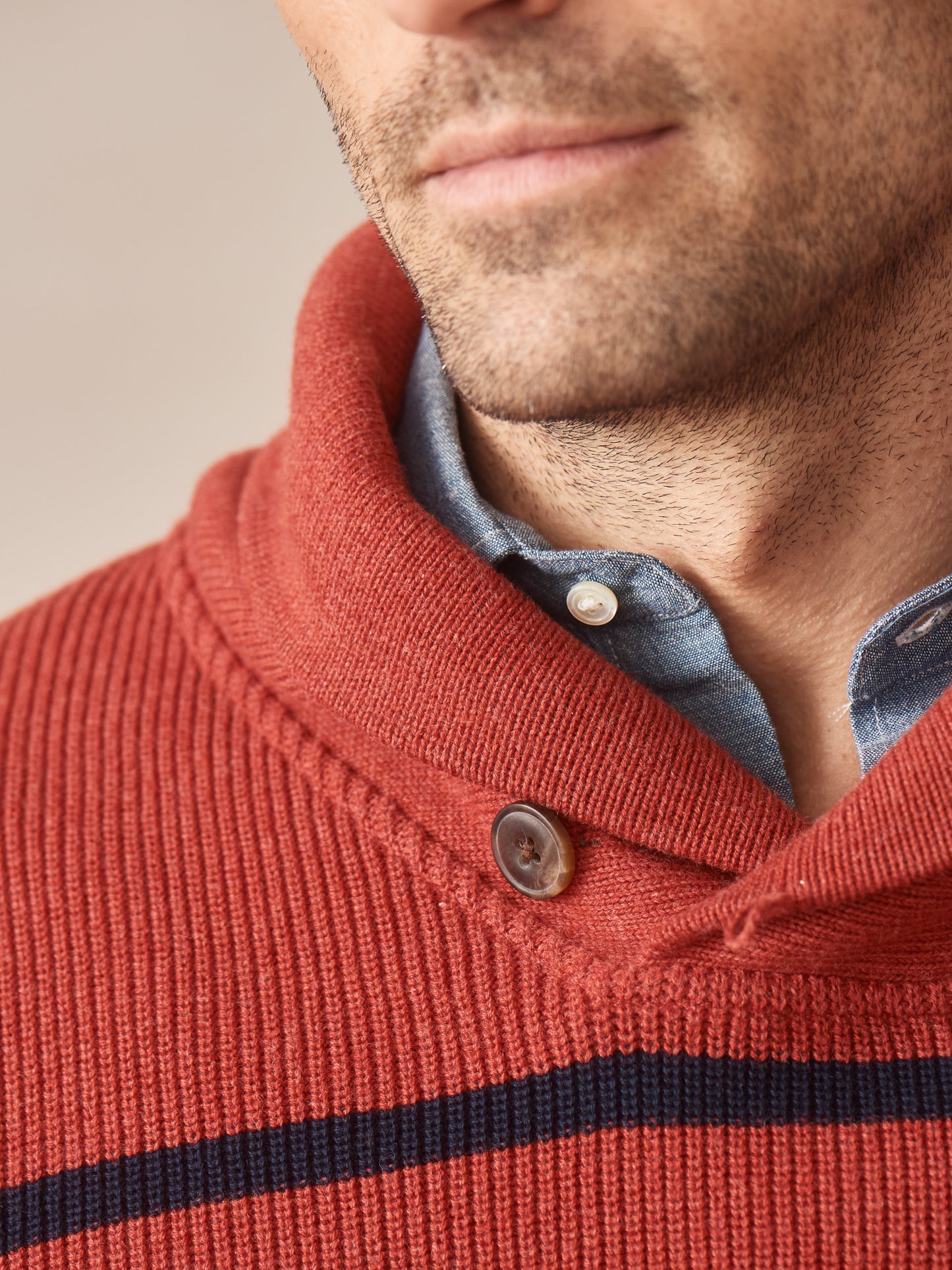 Close-up of a man wearing a rust-colored Hudson Sweater in Stripe by J.McLaughlin, layered over a denim shirt, showcasing effortlessly stylish, enduring designs in innovative fabrics.