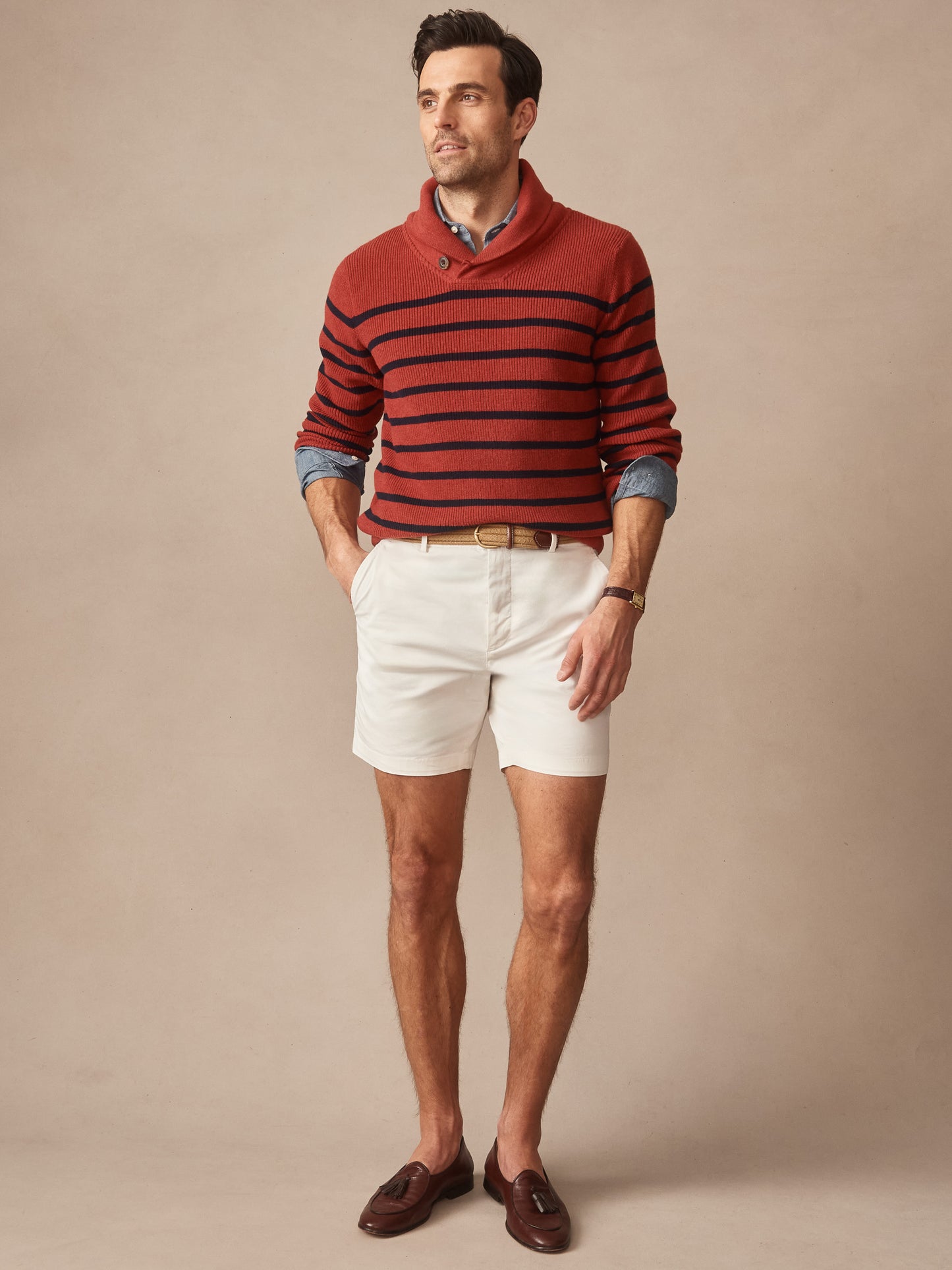 Man wearing a J. McLaughlin Hudson Sweater in Stripe with red and navy horizontal stripes, paired with beige shorts and brown loafers, showcasing effortlessly stylish, enduring designs.