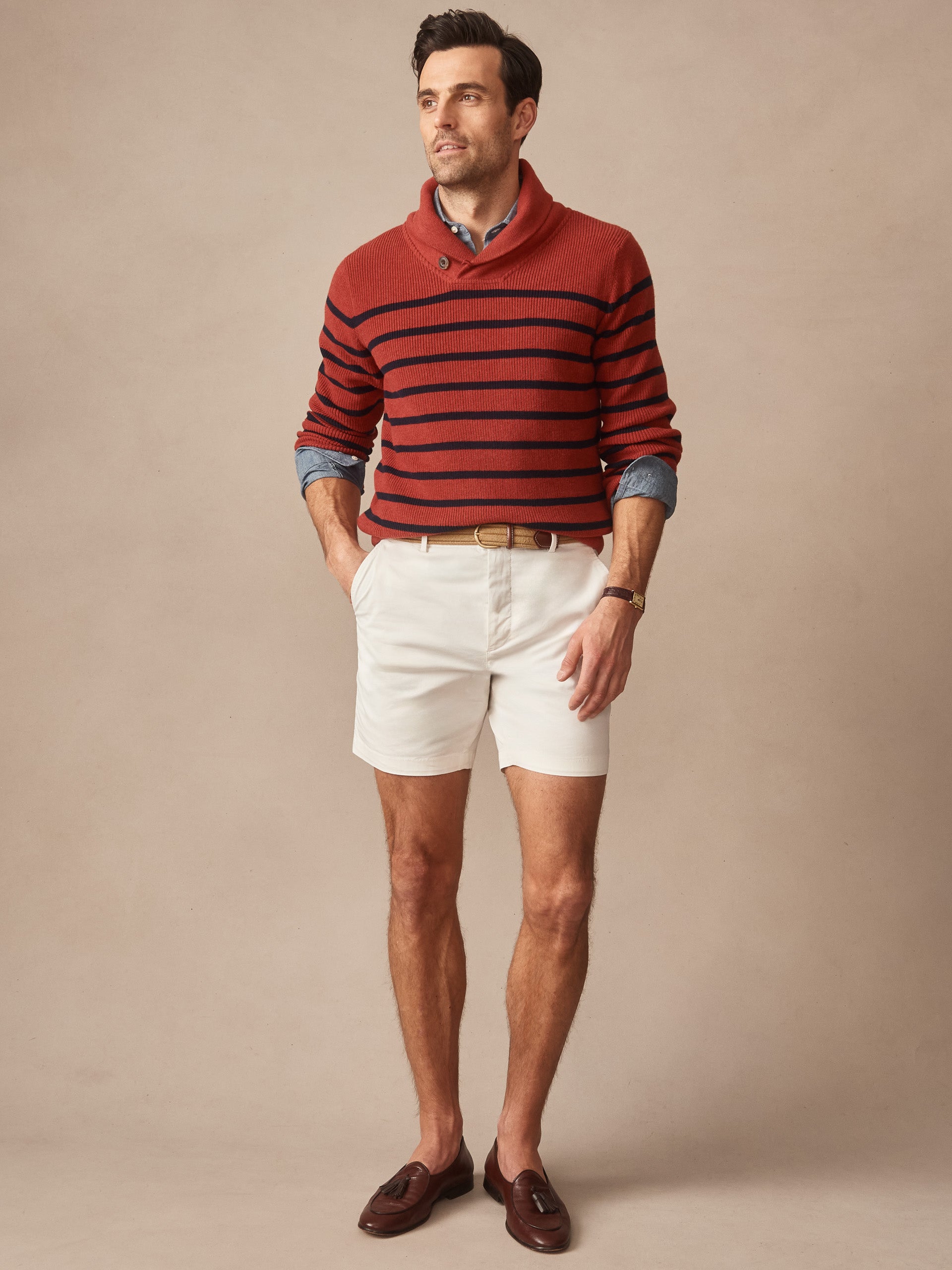 Man wearing a J. McLaughlin Hudson Sweater in Stripe with red and navy horizontal stripes, paired with beige shorts and brown loafers, showcasing effortlessly stylish, enduring designs.