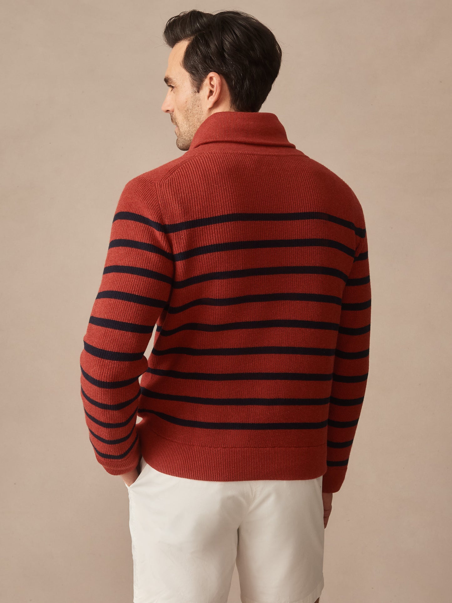Man wearing a rust-colored Hudson Sweater in Stripe with navy horizontal stripes, paired with white shorts, showcasing effortlessly stylish, enduring designs by J.McLaughlin.