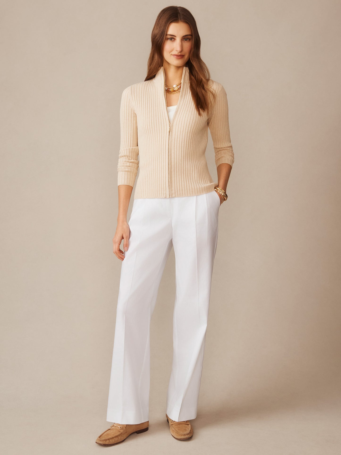Woman wearing a J.McLaughlin Clemence Zip Cardigan in a soft oatmeal tone paired with white trousers and loafers, reflecting effortlessly stylish, enduring designs and innovative fabrics.