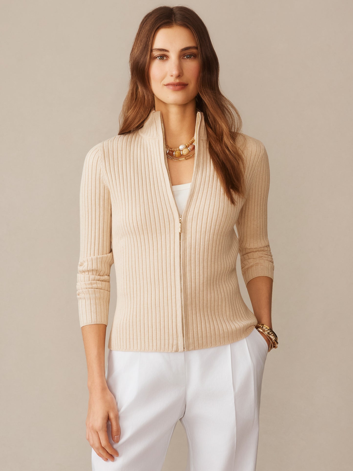 Woman wearing Clemence Zip Cardigan in oatmeal by J.McLaughlin, styled with white pants and layered necklaces, showcasing effortlessly stylish and enduring designs in a timeless look.