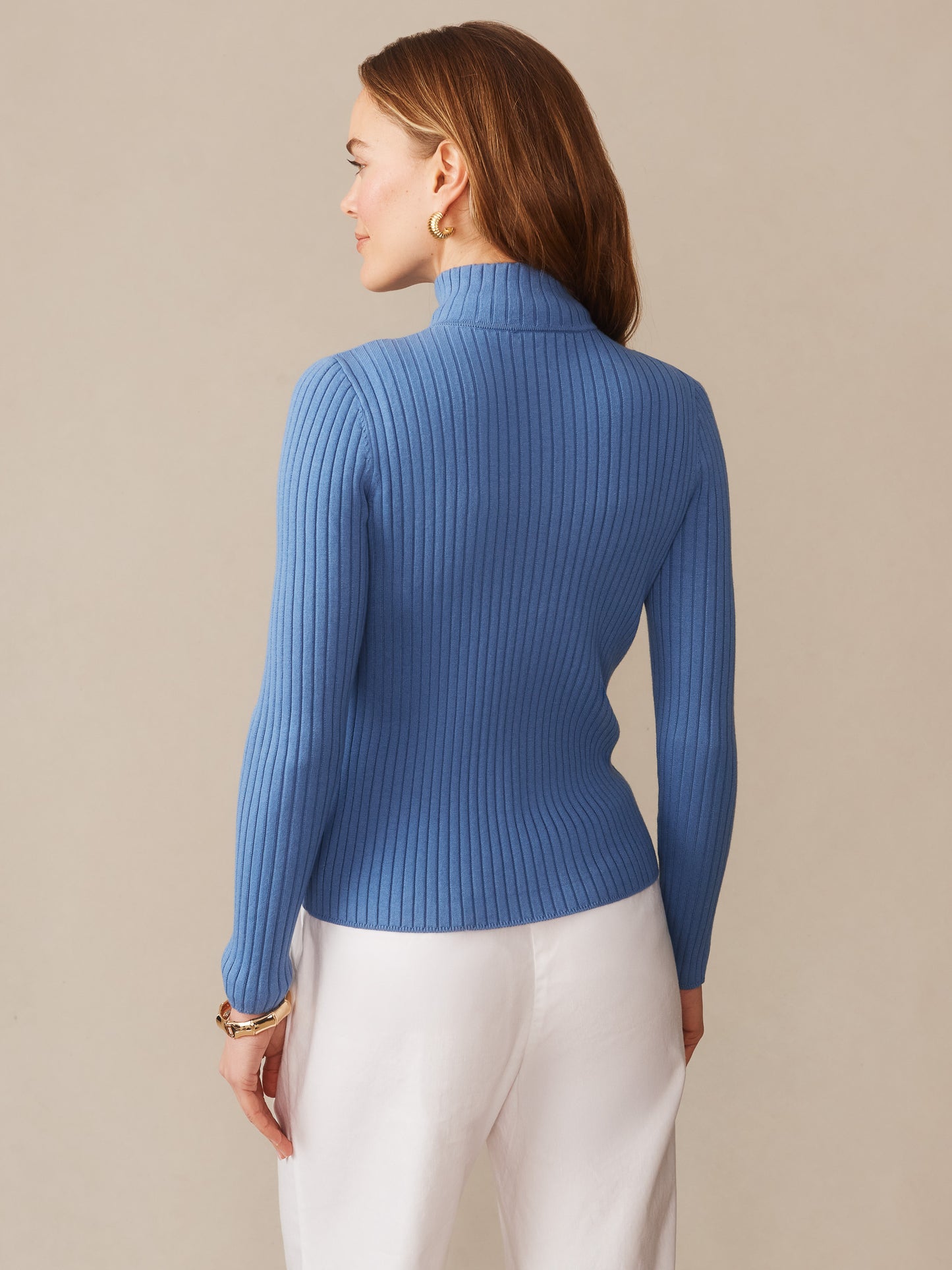Woman seen from behind wearing a ribbed blue Clemence Zip Cardigan by J.McLaughlin paired with white pants, showcasing effortlessly stylish, enduring designs and innovative fabrics.