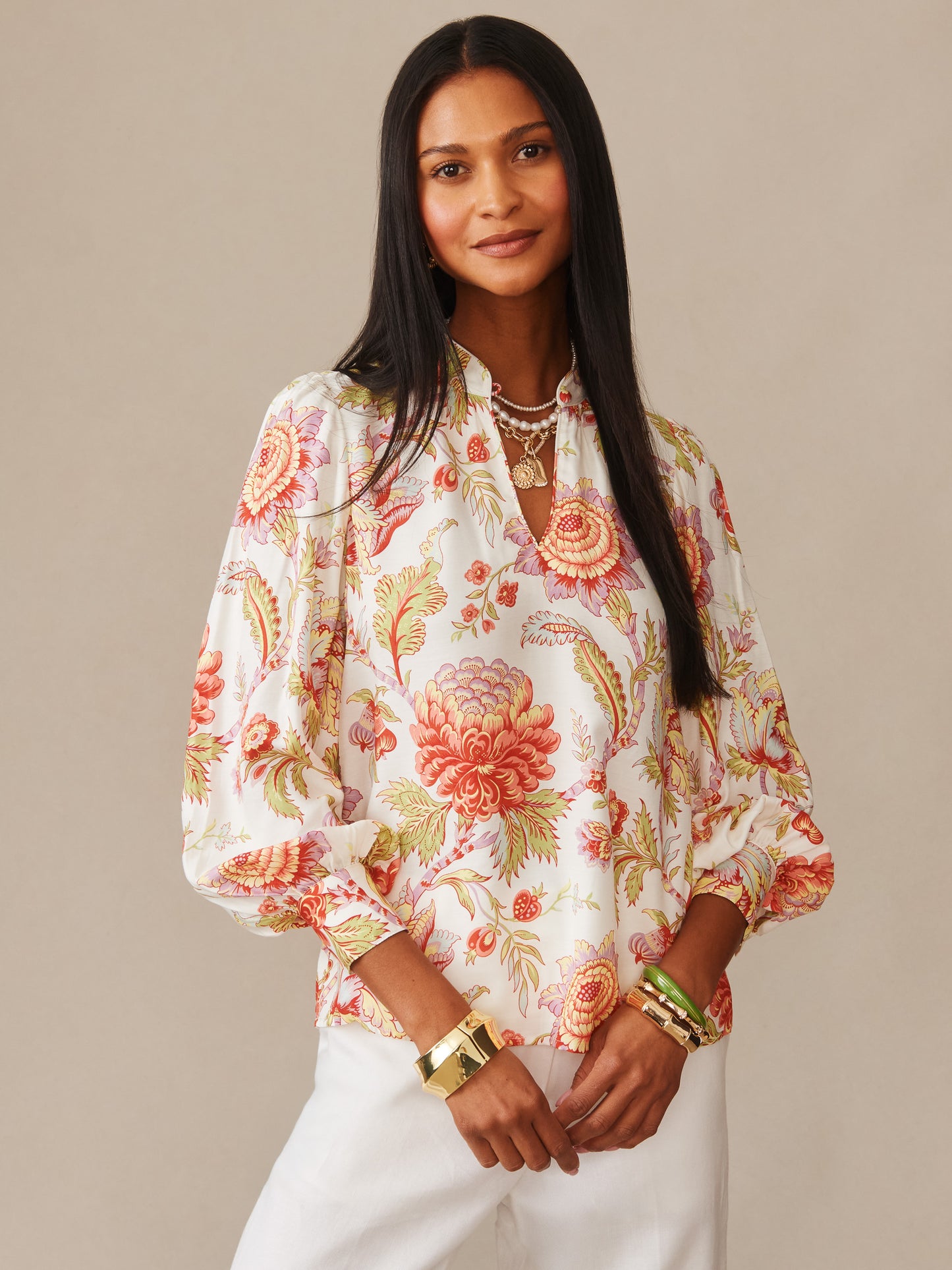 Woman wearing a Maeve Silk Blend Blouse in Cerulean Garden by J.McLaughlin, featuring a floral pattern with warm tones, paired with white pants and gold jewelry, embodying effortlessly stylish, enduring designs with innovative fabrics for a legacy of timeless fashion at a destination for defining style. Life, Well-Lived.