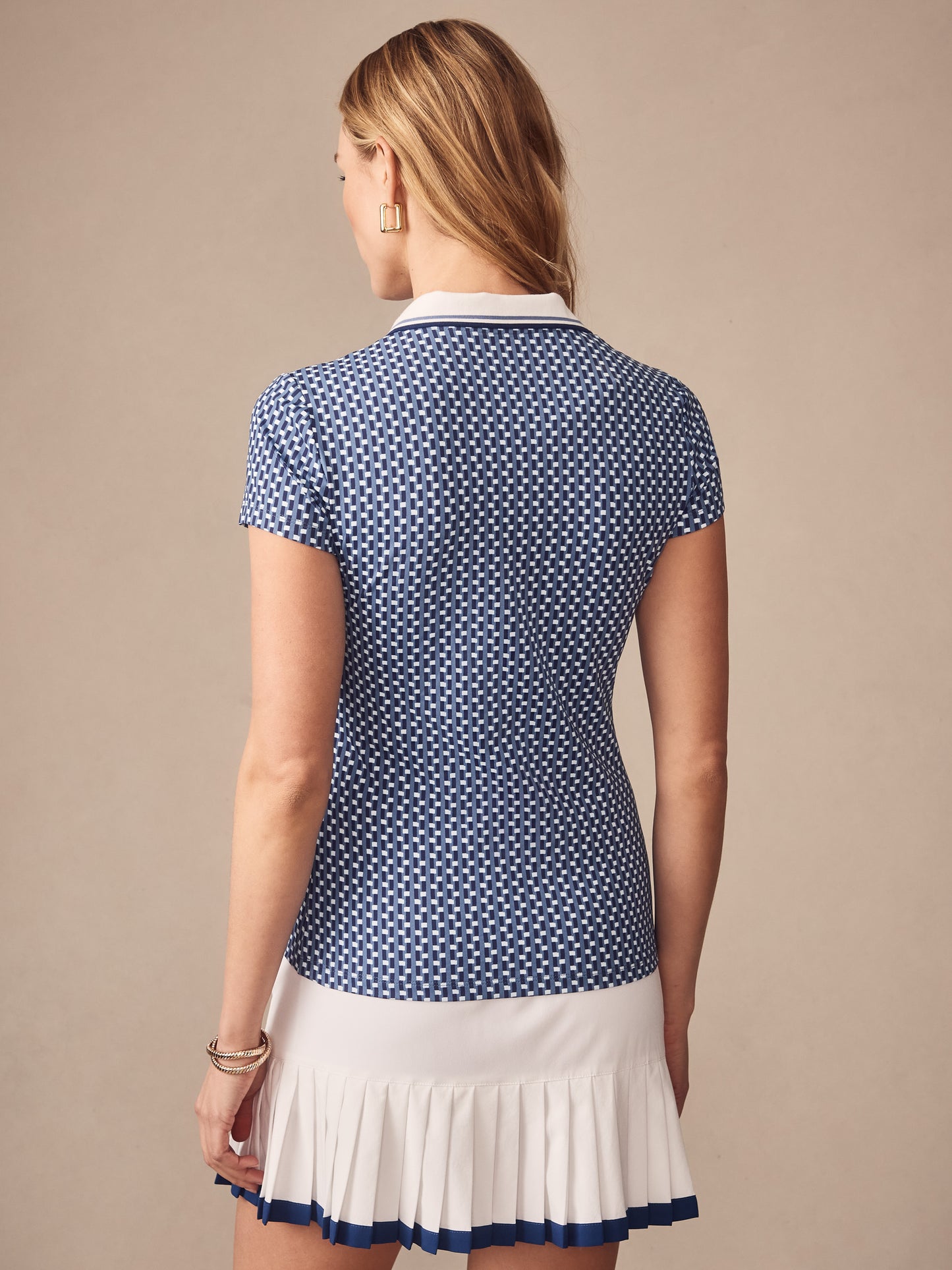 Woman wearing Court Cap Sleeve Polo in Azrou by J. McLaughlin, featuring a blue and white geometric pattern with a white collar, paired with a white pleated skirt with blue trim, showcasing effortlessly stylish, enduring designs and innovative fabrics for a legacy of timeless fashion at a destination for defining style. Life, Well-Lived.