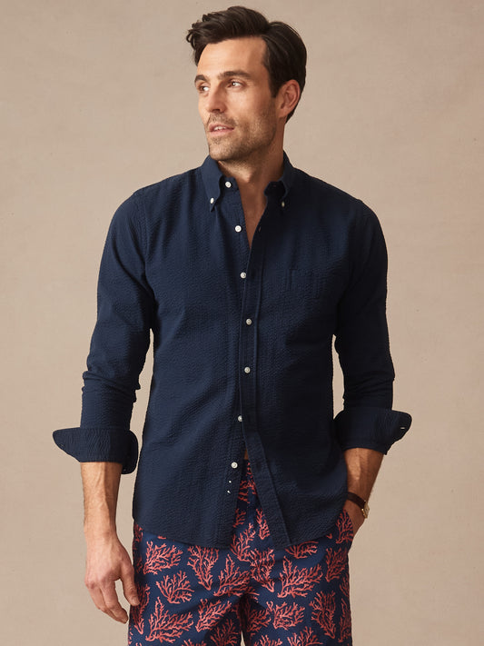 Man wearing a navy Belvedere Cotton Seersucker Shirt by J.McLaughlin paired with coral patterned shorts, showcasing effortlessly stylish and enduring designs for a life well-lived.