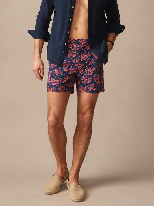 Man wearing Deck Swim Trunks in Midi Coral Cay Texture by J.McLaughlin styled with a navy shirt and beige slip-on shoes, showcasing effortlessly stylish swimwear with enduring designs.