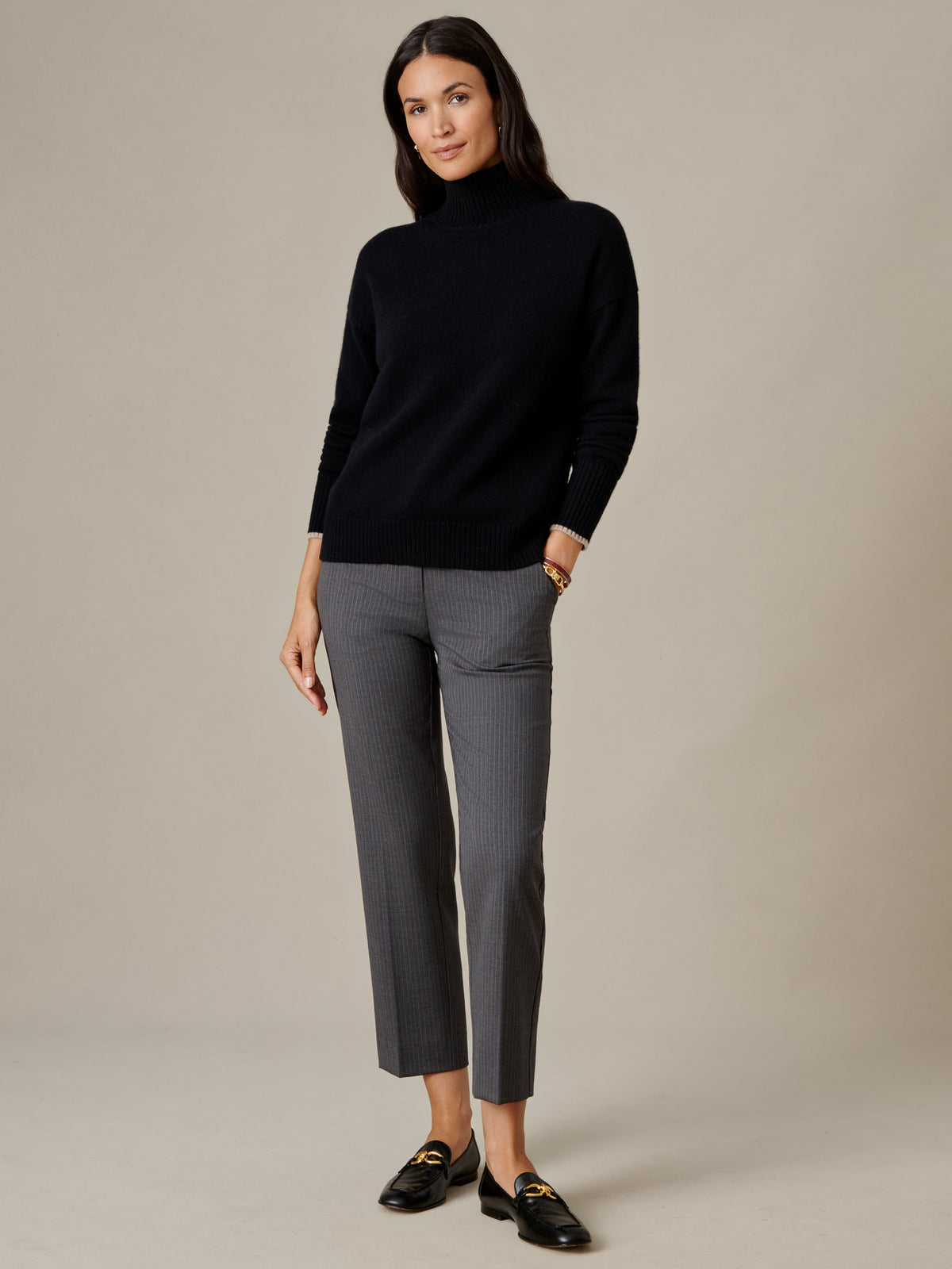 J.McLaughlin Dina Cashmere Turtleneck in black styled with gray pants and black loafers on a model in a refined studio setting