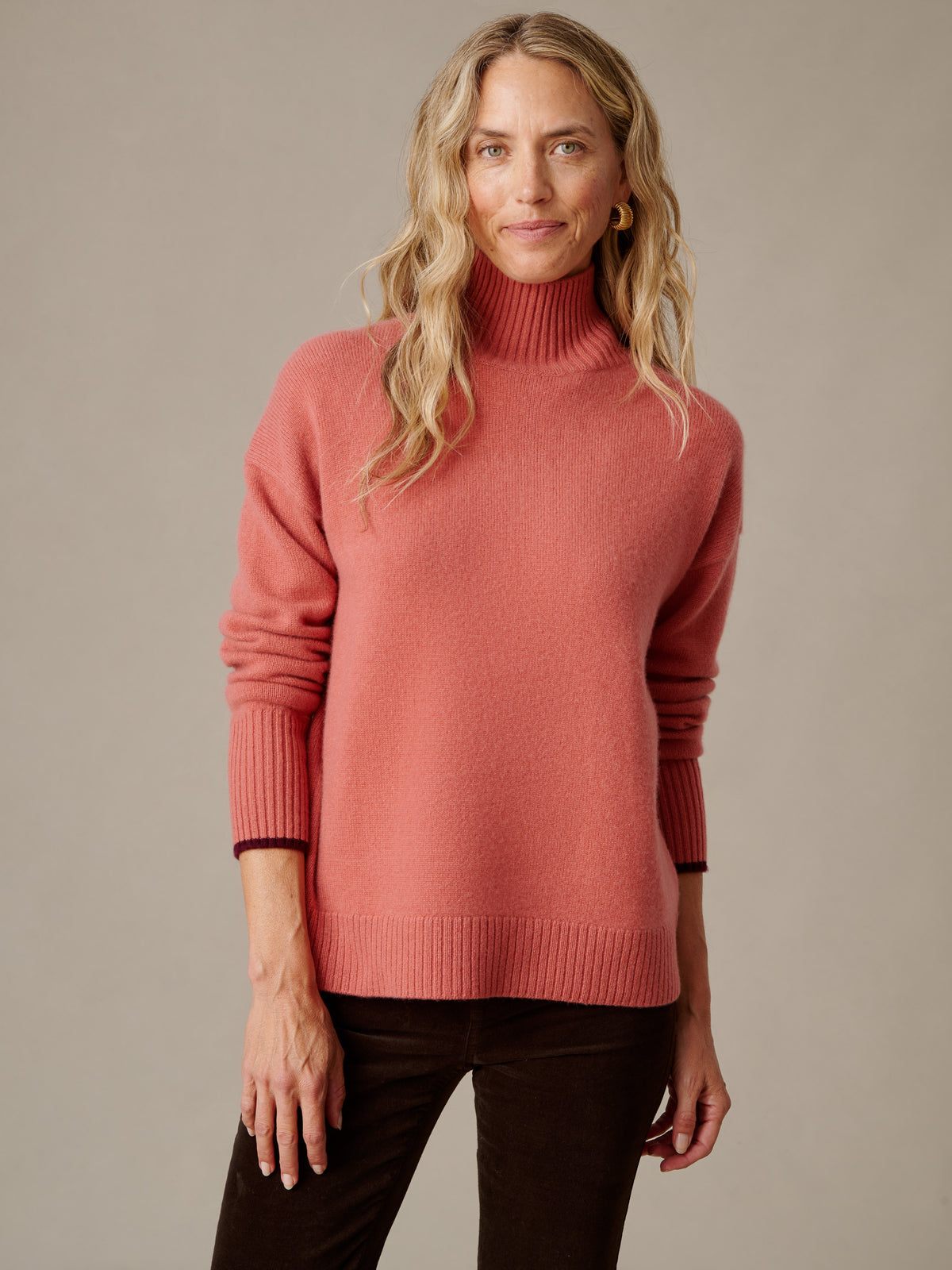 Dina Cashmere Turtleneck by J.McLaughlin in coral with a ribbed collar and cuffs modeled with dark pants by a woman