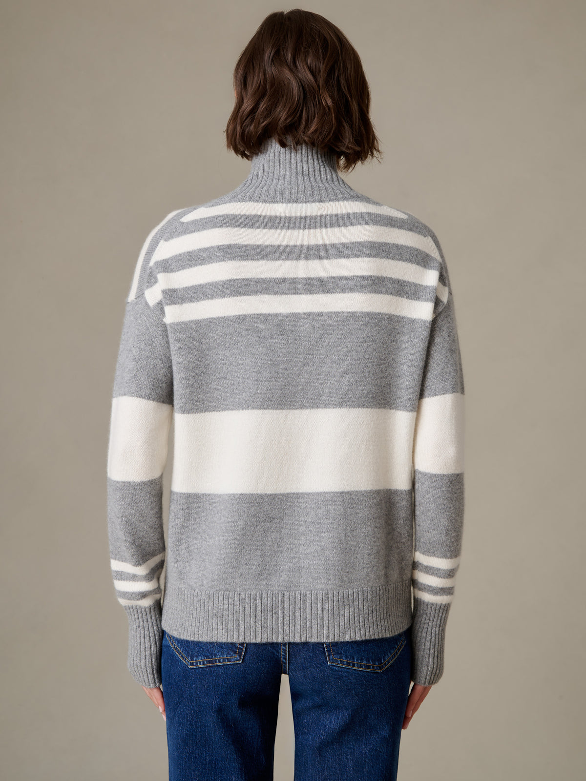 Dina Cashmere Turtleneck in Stripe by J.McLaughlin shown from the back with gray and cream horizontal stripes ribbed cuffs and hem worn with blue jeans
