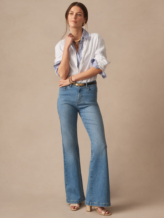 Woman wearing Domino Jeans by J.McLaughlin in light denim with a white blouse and striped shirt cuffs, styled with gold accessories, showcasing effortlessly stylish, enduring designs.