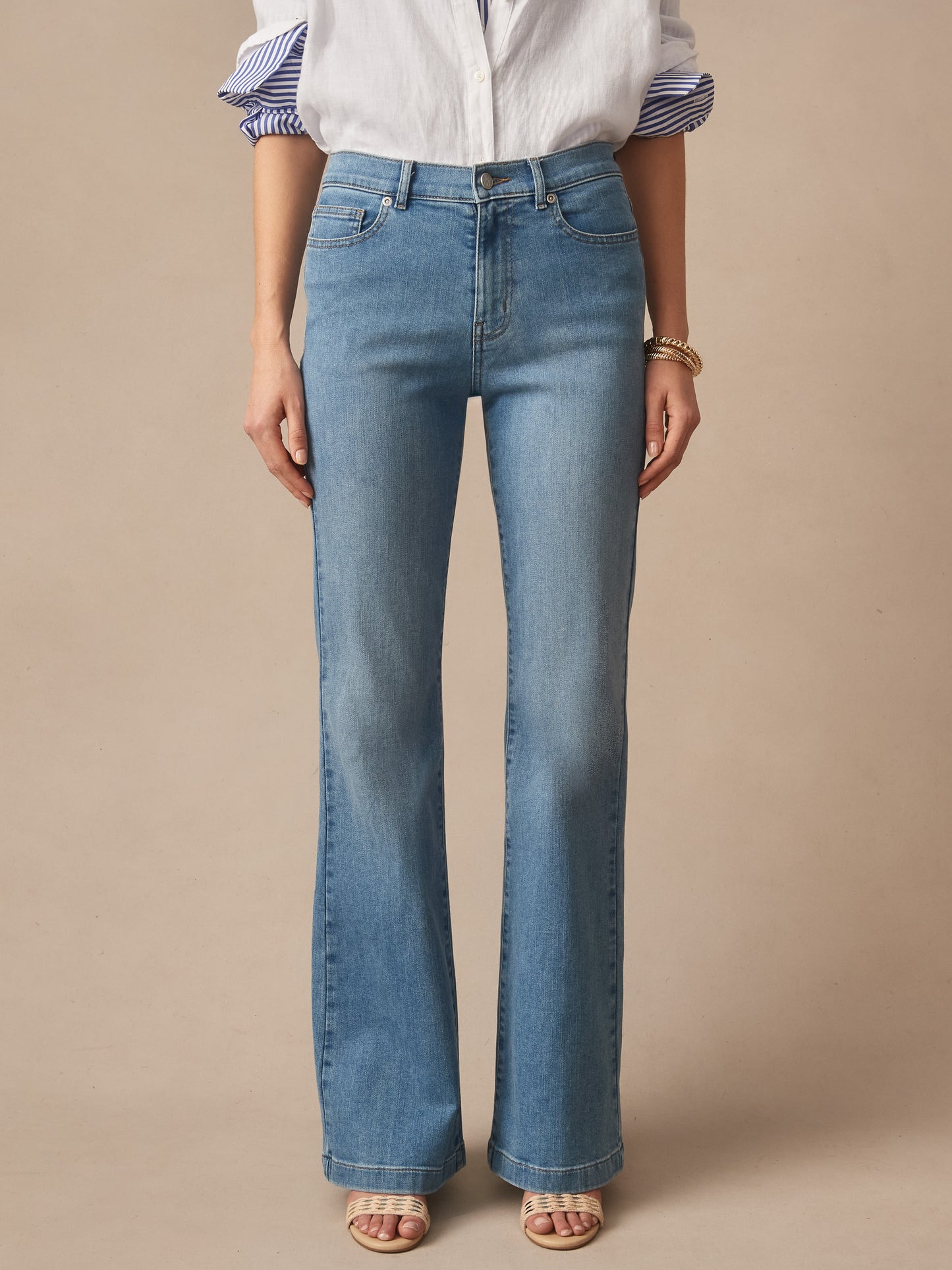 Front view of a person wearing light blue Domino Jeans by J.McLaughlin, paired with a white blouse and open-toe sandals, showcasing effortlessly stylish denim with enduring designs in an innovative fabric, reflecting a legacy of timeless fashion from a destination for defining style. Life, Well-Lived.