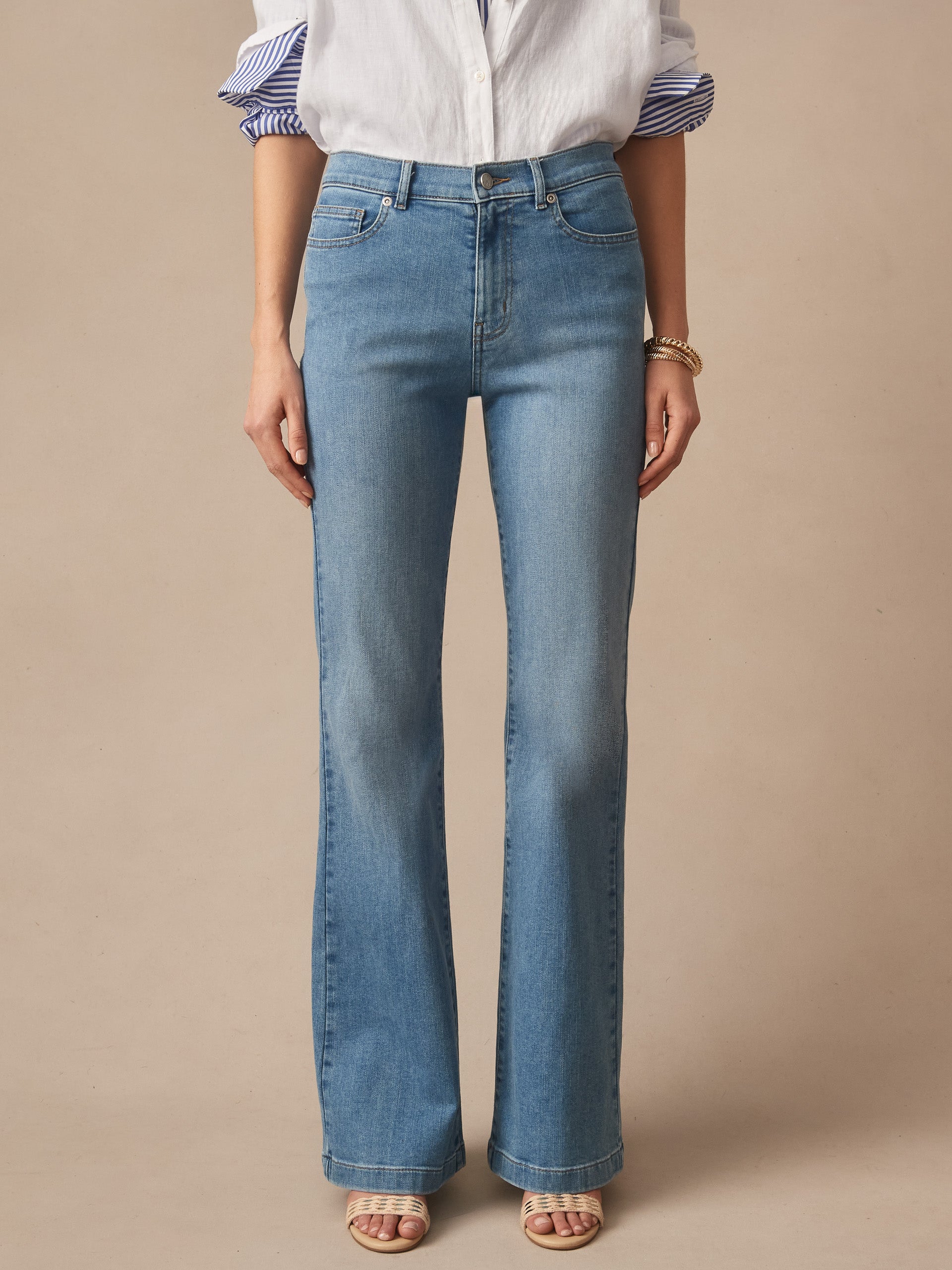 Front view of a person wearing light blue Domino Jeans by J.McLaughlin, paired with a white blouse and open-toe sandals, showcasing effortlessly stylish denim with enduring designs in an innovative fabric, reflecting a legacy of timeless fashion from a destination for defining style. Life, Well-Lived.