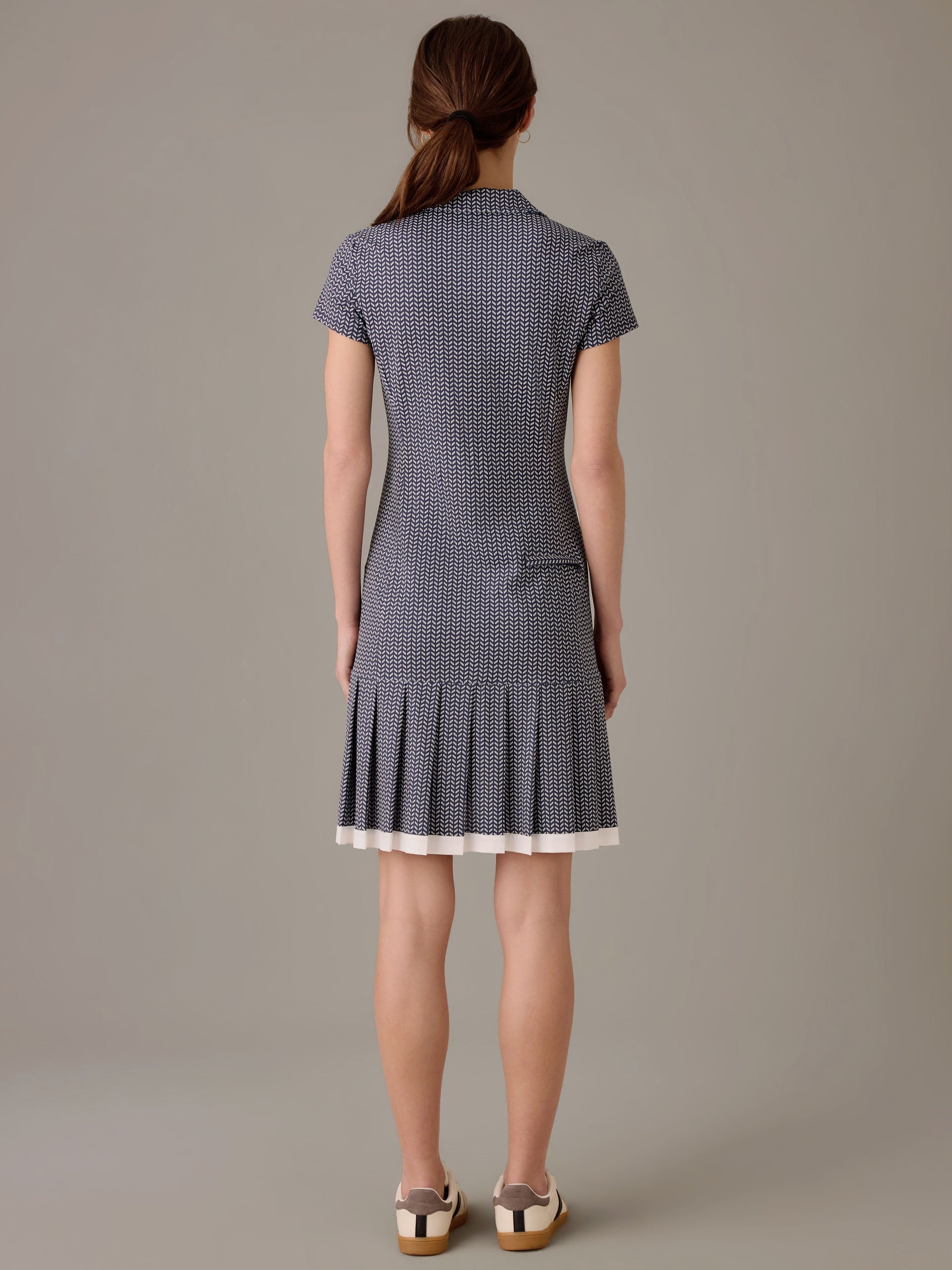 A woman wearing the Dorte Dress in Vine by J.McLaughlin, featuring a fitted silhouette with short sleeves and a pleated hem, styled with casual shoes.
