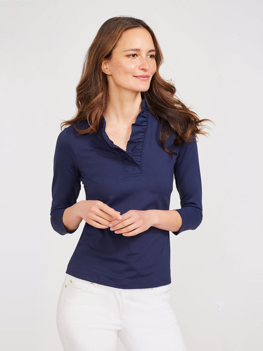 Woman wearing a navy Durham Ruffle Top by J.McLaughlin with three-quarter sleeves and delicate ruffle detail along the neckline, paired with white pants.