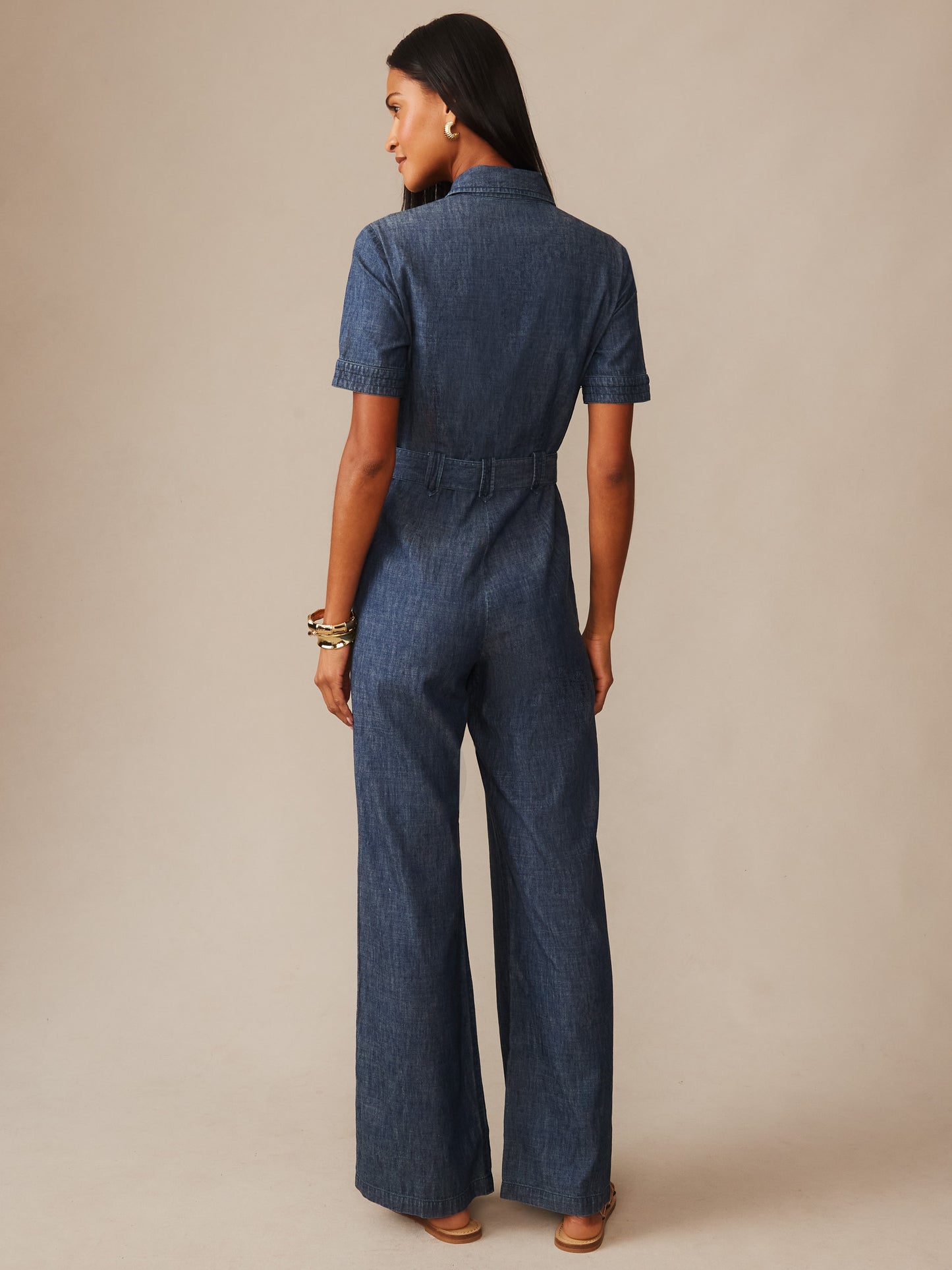 Woman wearing a blue denim Elena Jumpsuit from J.McLaughlin, featuring short sleeves and wide-leg pants, showcasing effortlessly stylish and enduring designs for a life well-lived.