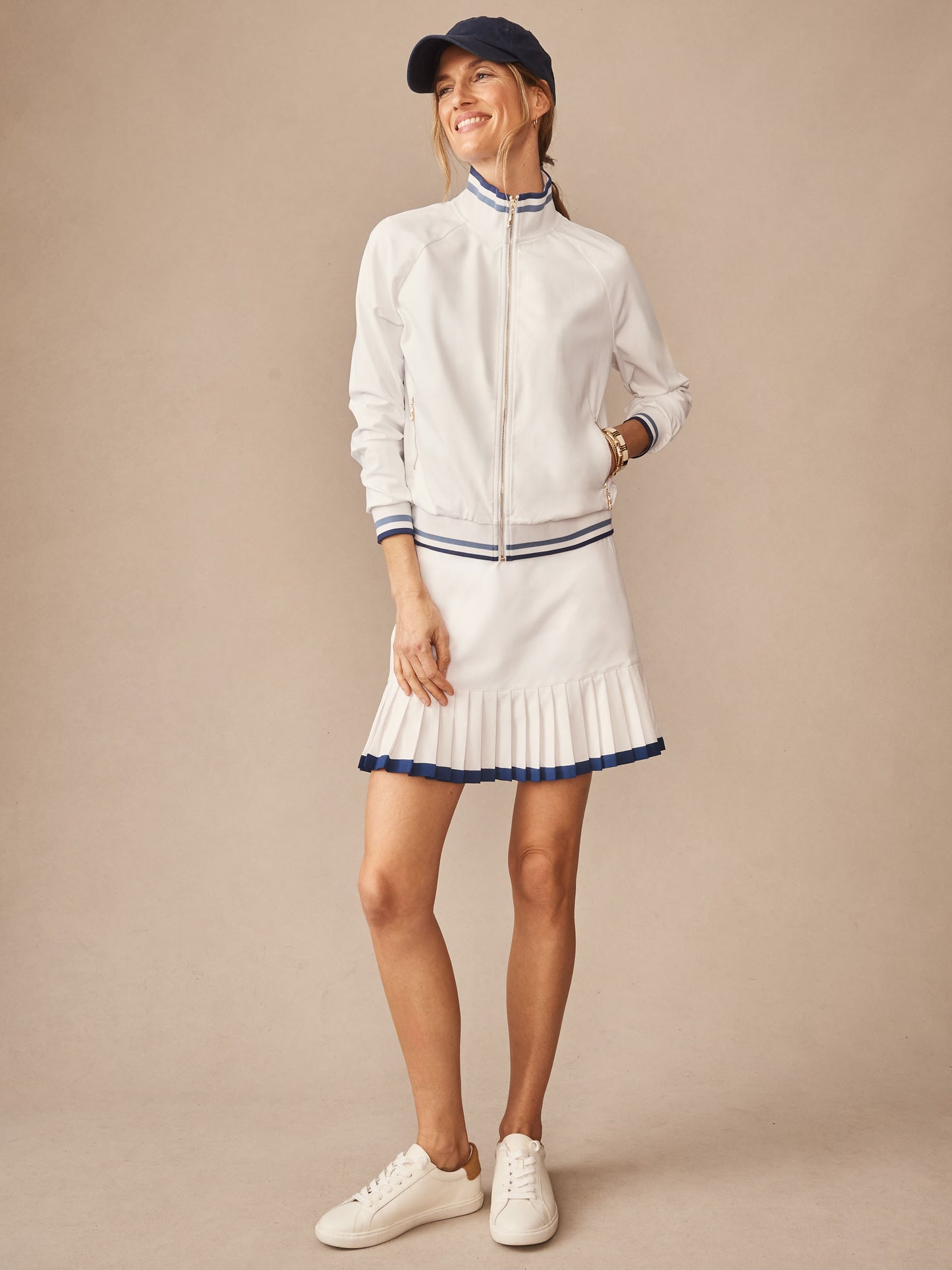 Woman wearing the Elettra Jacket by J.McLaughlin, styled with a pleated skirt and cap, showcasing effortlessly stylish and enduring designs crafted with innovative fabrics for a legacy of timeless fashion. A destination for defining style. Life, Well-Lived.