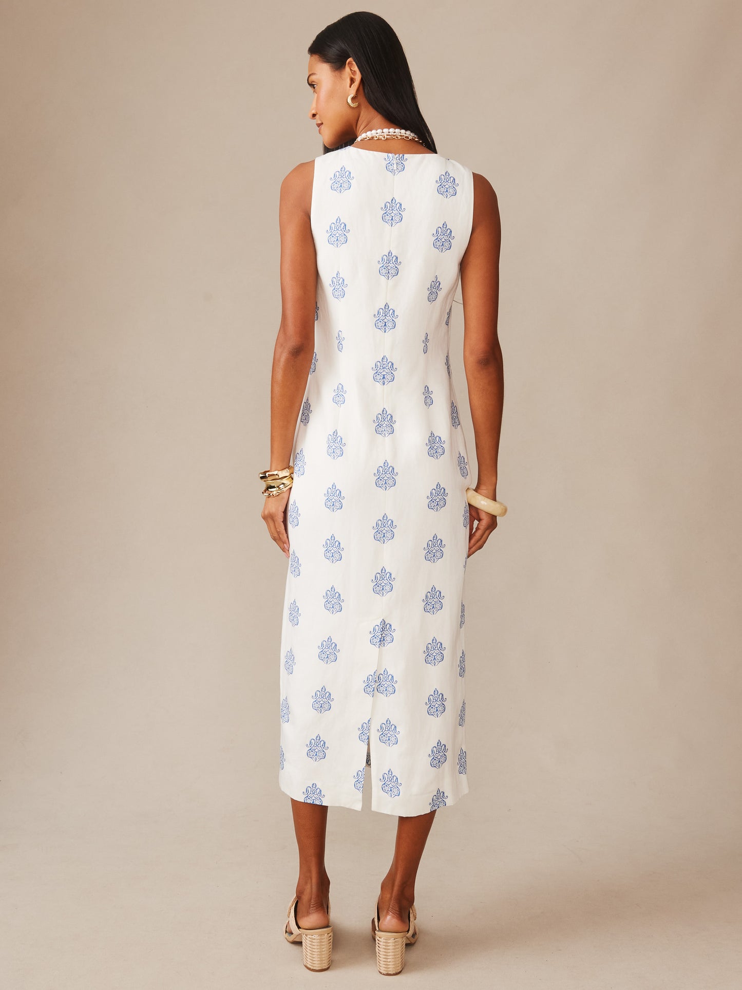 A woman models the back of the Ella Linen Blend Dress in Apertivo by J.McLaughlin, featuring a sleeveless white design with a subtle blue pattern, embodying effortlessly stylish and enduring designs.