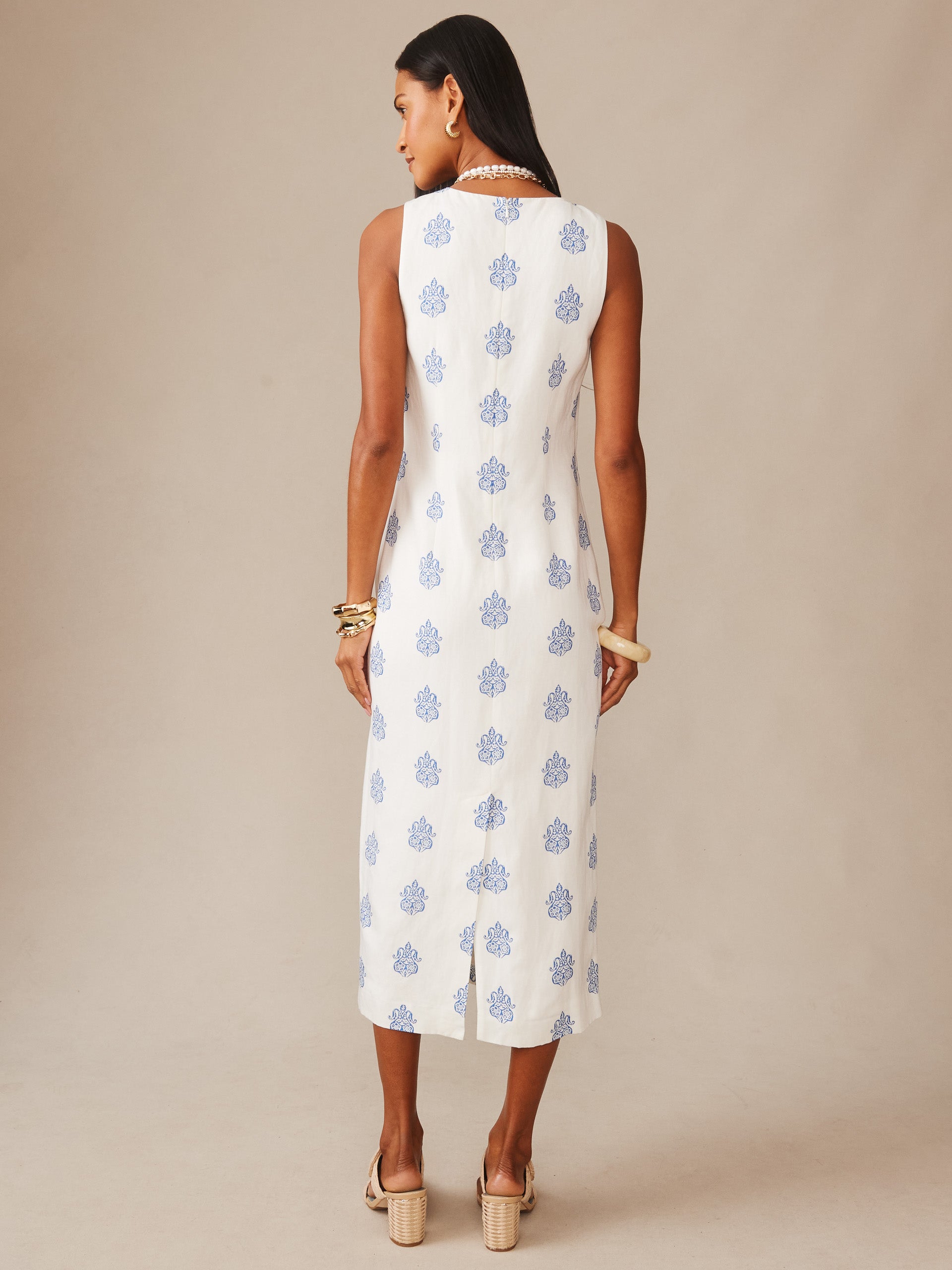 A woman models the back of the Ella Linen Blend Dress in Apertivo by J.McLaughlin, featuring a sleeveless white design with a subtle blue pattern, embodying effortlessly stylish and enduring designs.