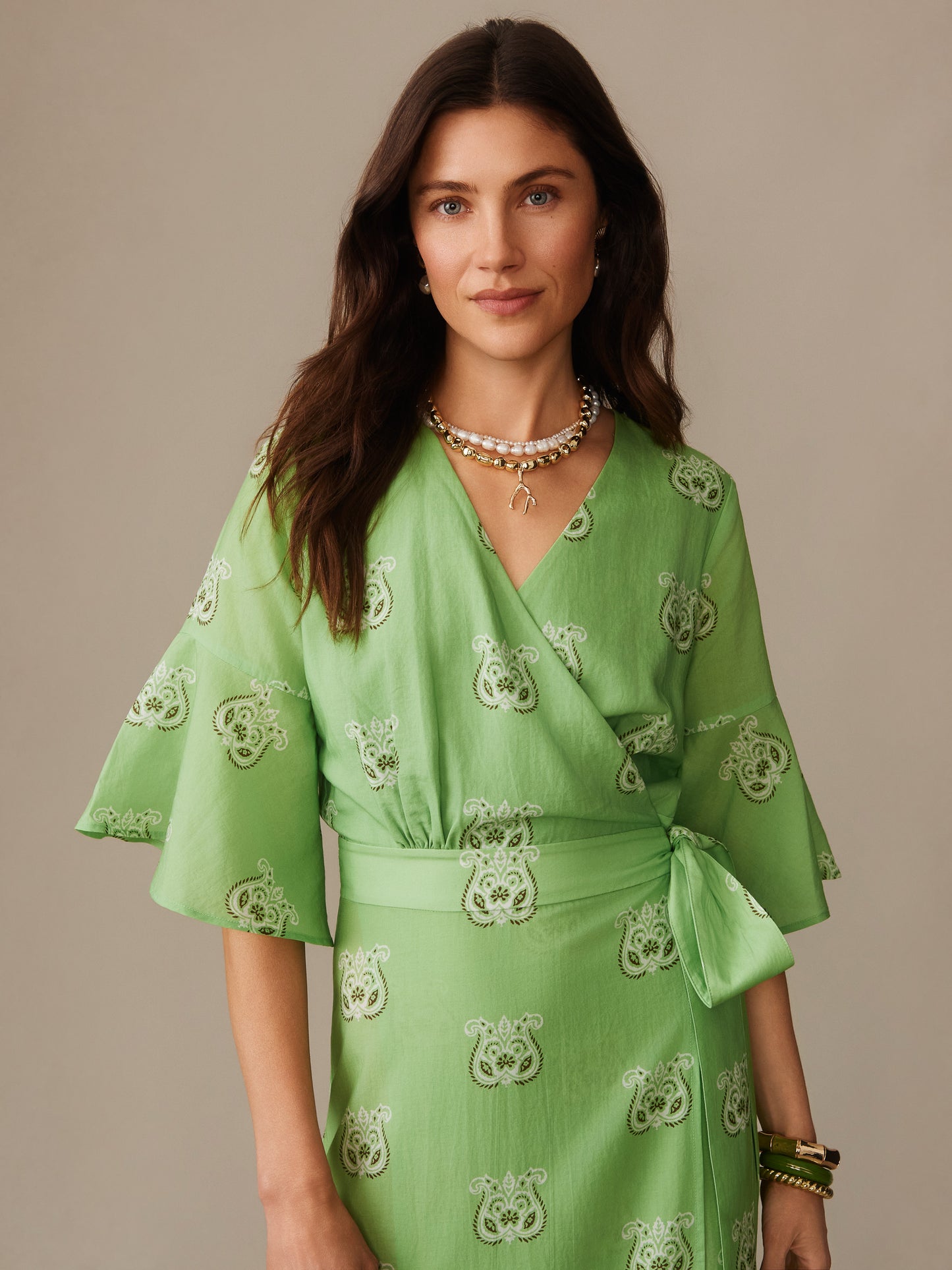 Woman wearing a green Emily Wrap Dress in Siesta by J.McLaughlin featuring elegant patterns and a tied waist, exemplifying effortlessly stylish, enduring designs with innovative fabrics.