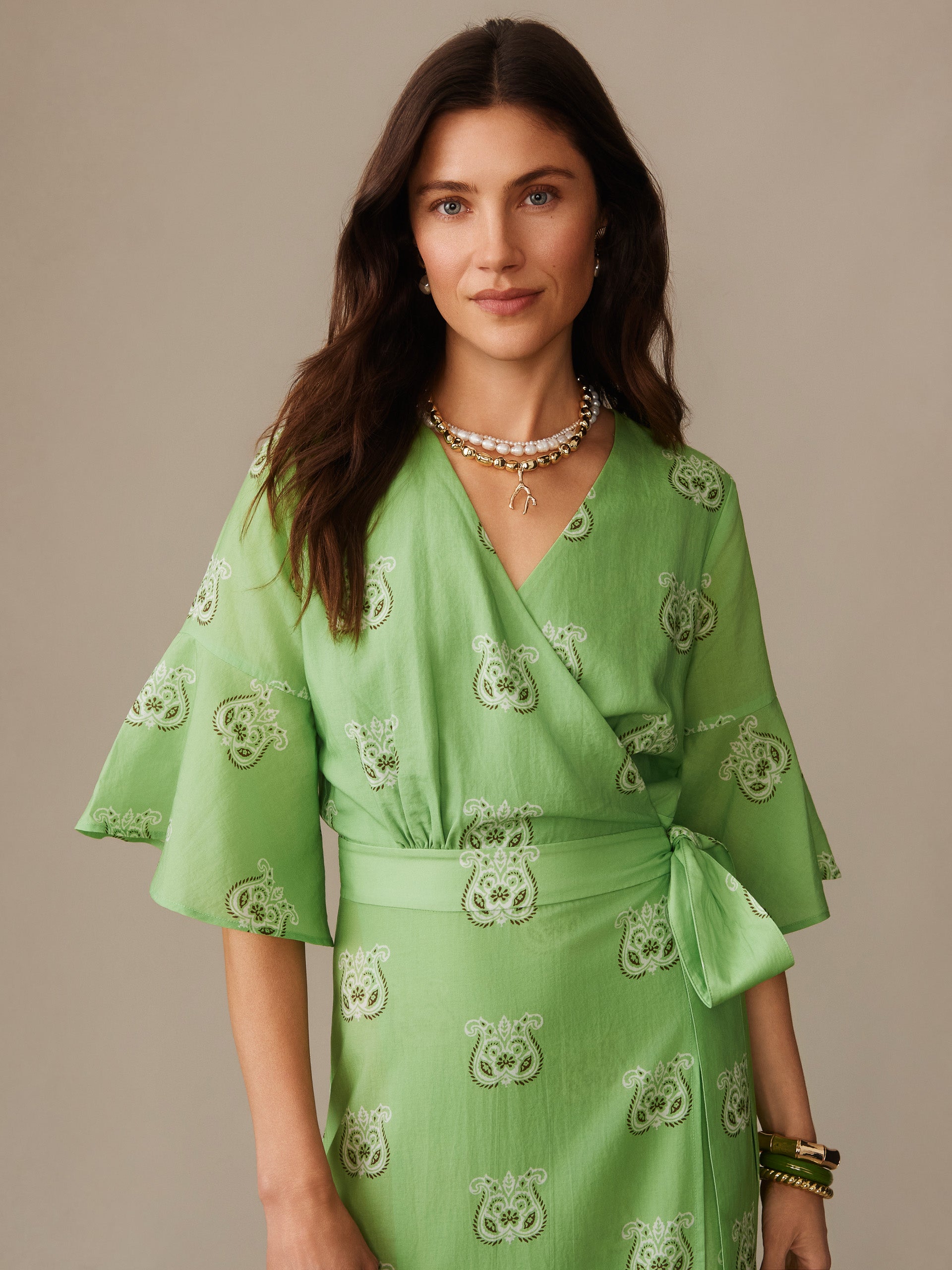 Woman wearing a green Emily Wrap Dress in Siesta by J.McLaughlin featuring elegant patterns and a tied waist, exemplifying effortlessly stylish, enduring designs with innovative fabrics.