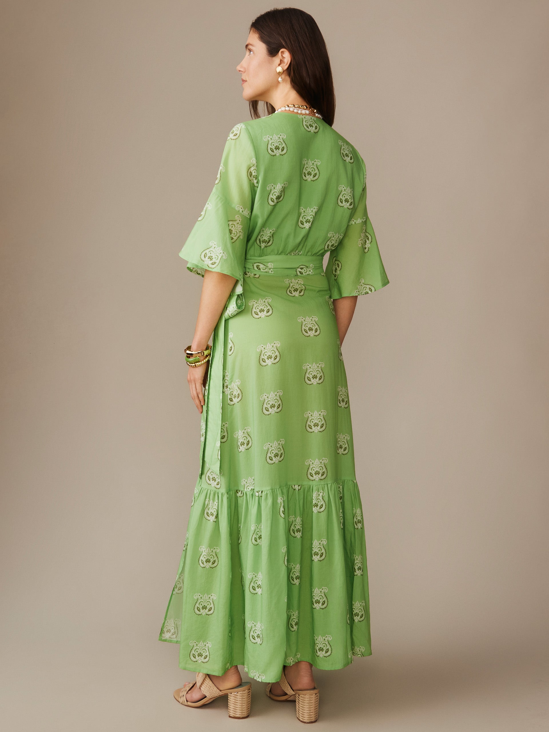 A woman wearing the Emily Wrap Dress in Siesta by J.McLaughlin, featuring an effortlessly stylish green pattern with elegant sleeves and a flowing skirt, embodying enduring designs and a legacy of timeless fashion, perfect for a destination for defining style. Life, Well-Lived.