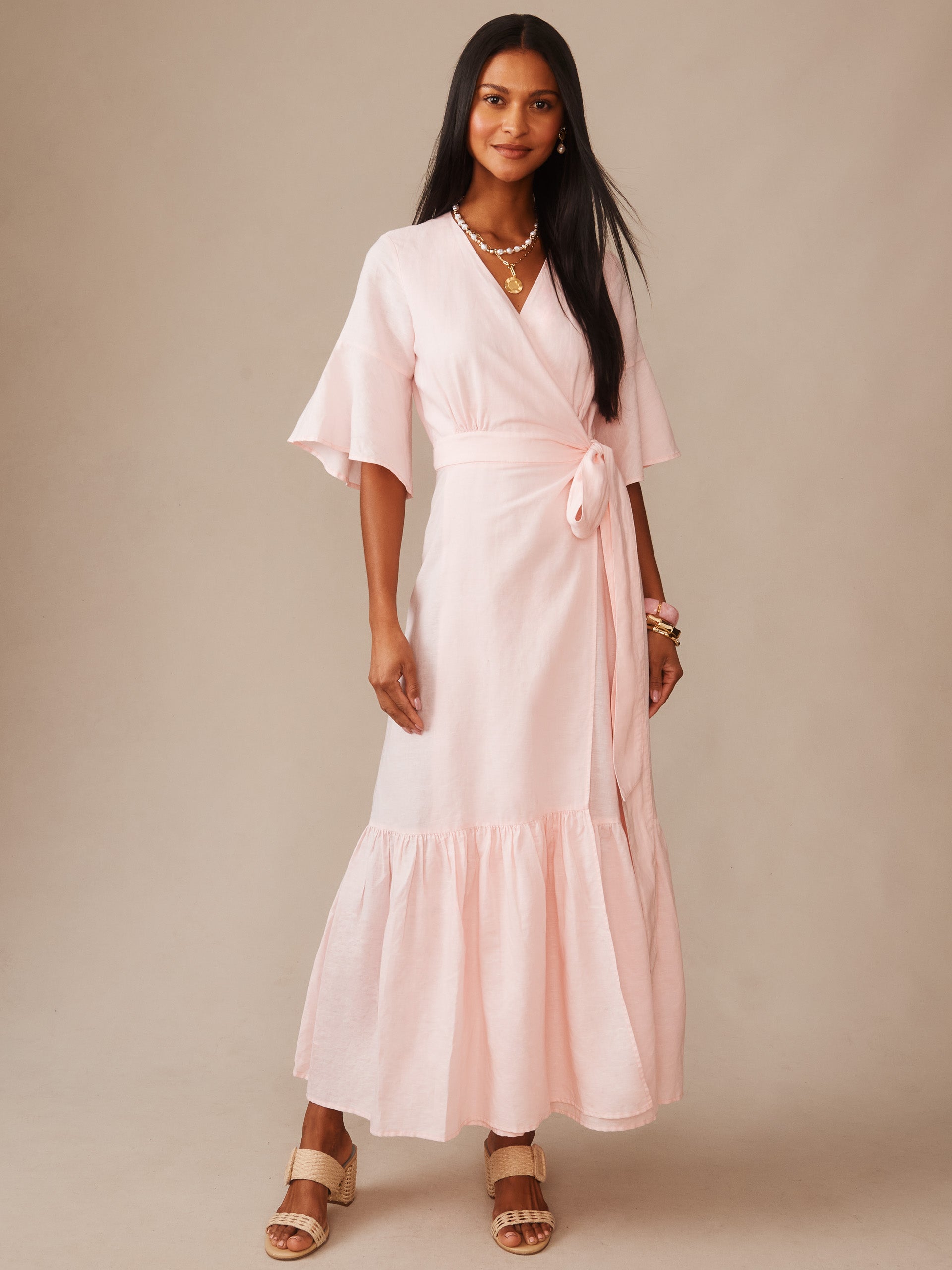 Woman wearing a light blush pink Emily Linen Blend Wrap Dress by J.McLaughlin, showcasing effortlessly stylish, enduring designs with a flattering tied waist and flowing skirt, perfect for a destination for defining style. Life, Well-Lived.