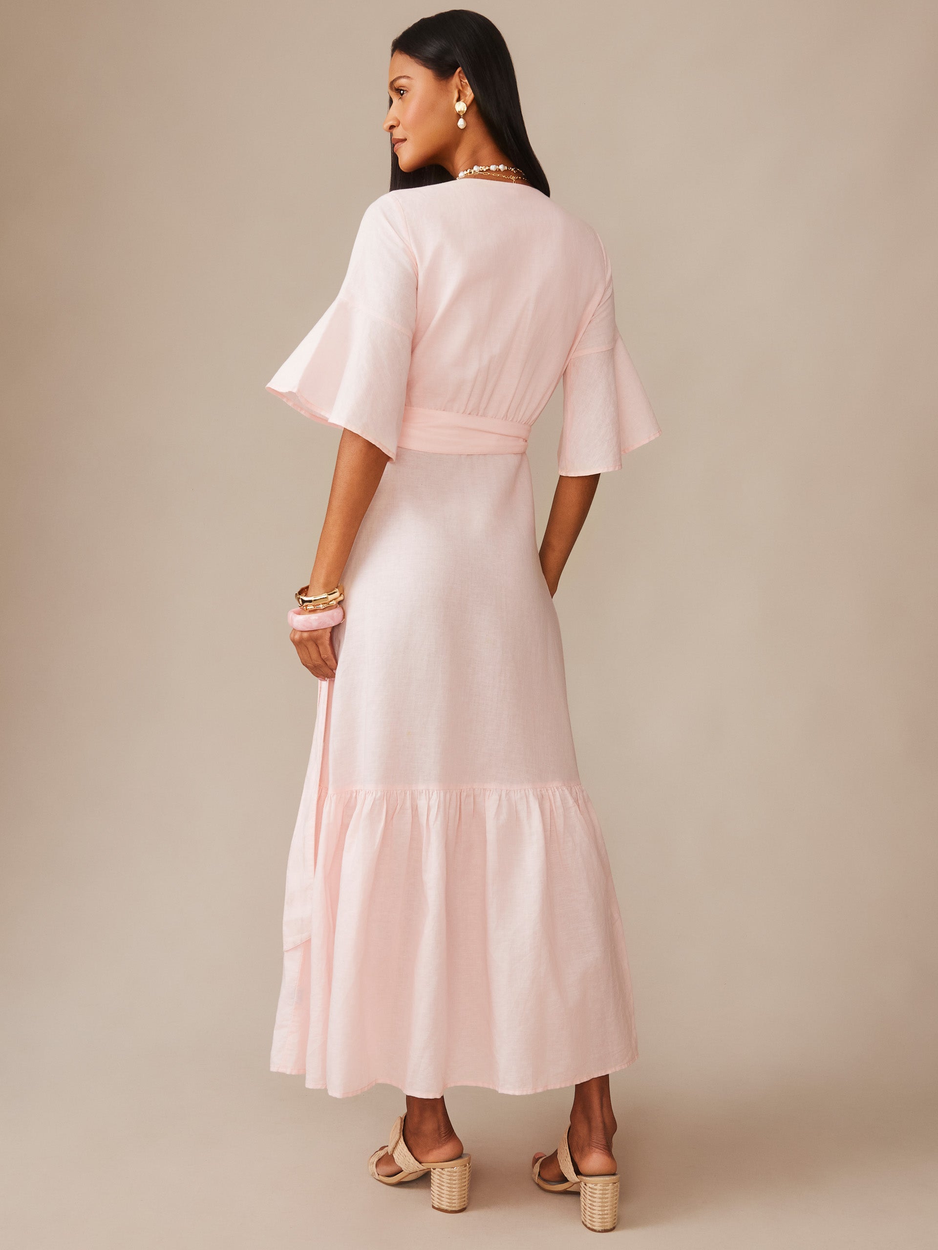 Woman wearing a light blush pink Emily Linen Blend Wrap Dress by J.McLaughlin with flared sleeves and a flowing skirt, embodying effortlessly stylish and enduring designs.