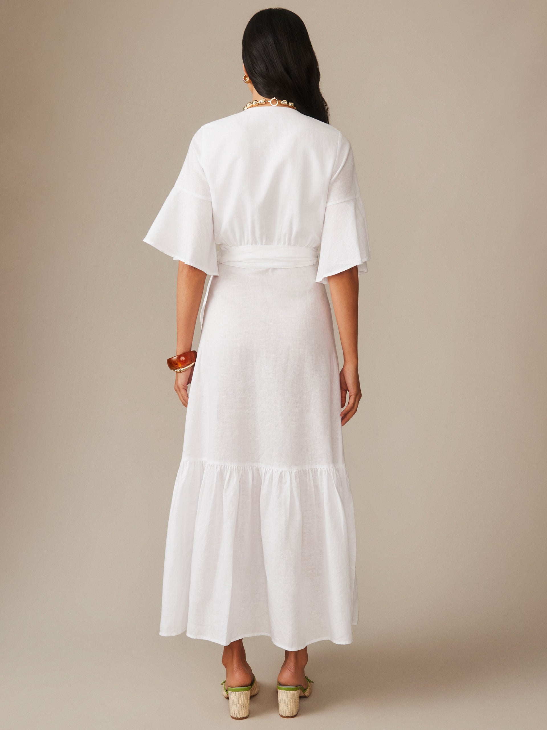 Woman wearing a white Emily Linen Blend Wrap Dress by J.McLaughlin, featuring flowing sleeves and a tiered skirt, showcasing effortlessly stylish, enduring designs with innovative fabrics.