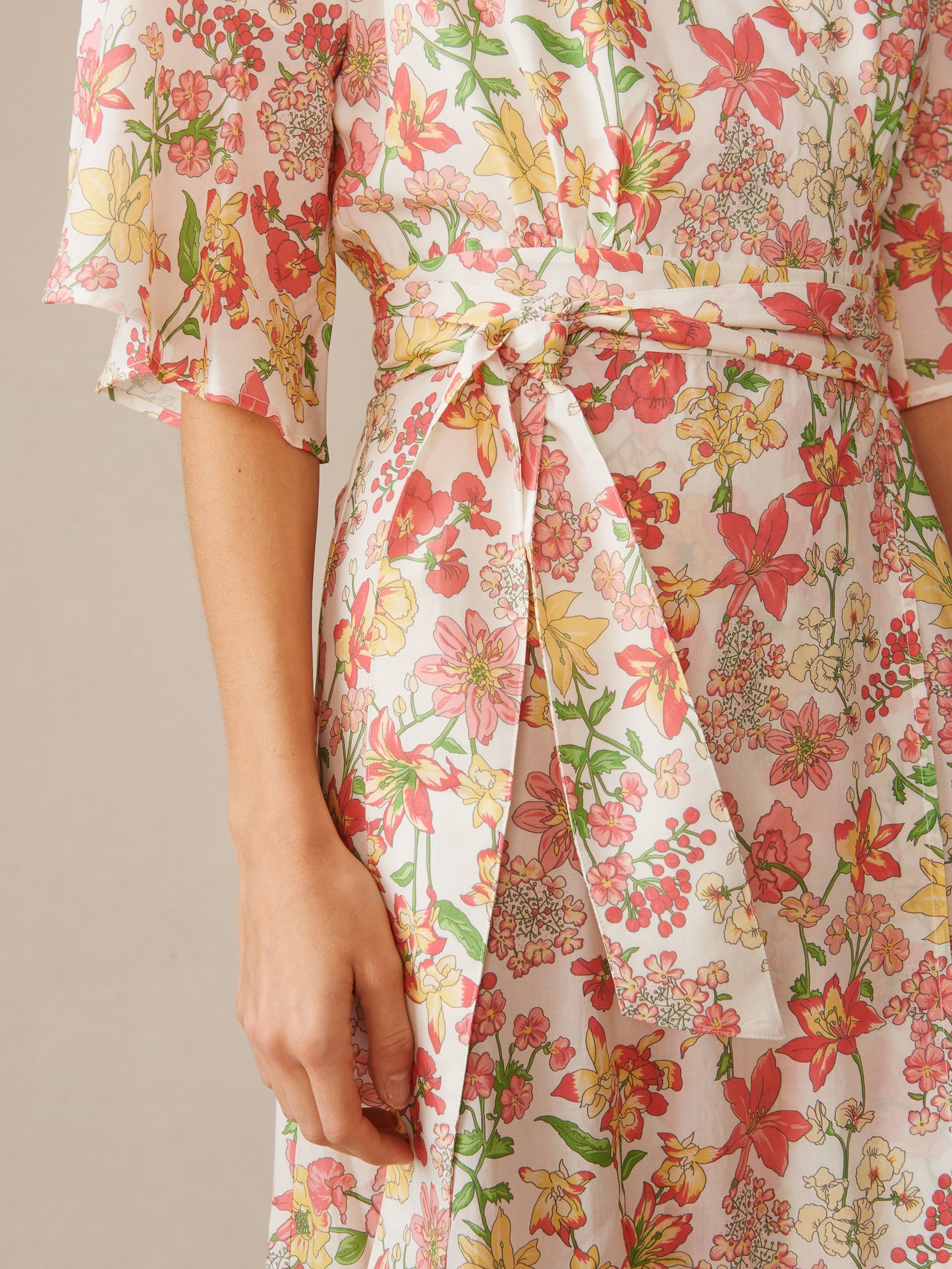 Close-up of a woman wearing the Emily Wrap Dress in Floral Villa by J.McLaughlin, featuring a delicate floral pattern with red, yellow, and green tones and a tied waist detail.