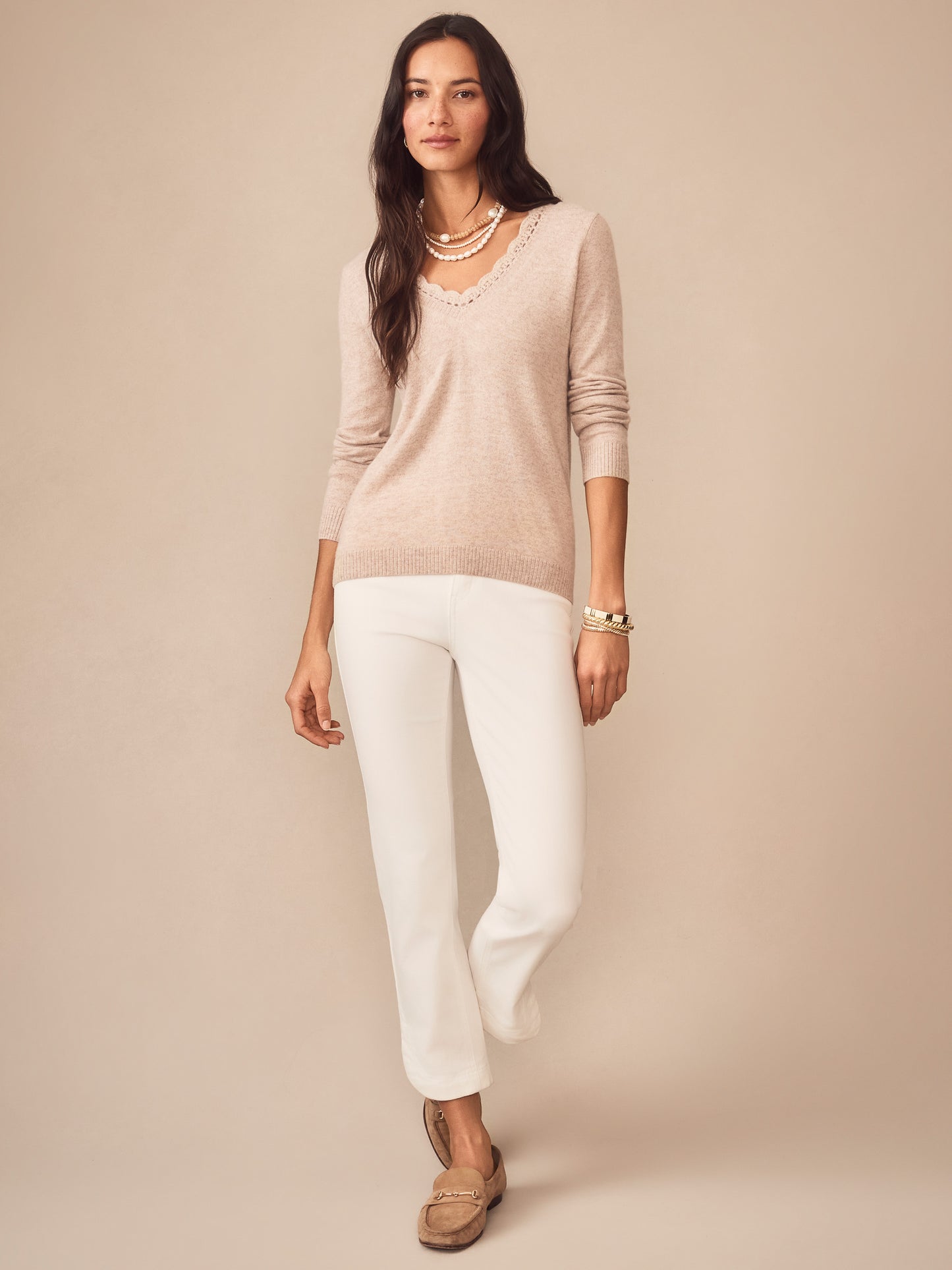 Woman wearing an oatmeal Evelyn Cashmere Sweater by J.McLaughlin paired with white pants and loafers, showcasing effortlessly stylish, enduring designs in luxurious fabric.