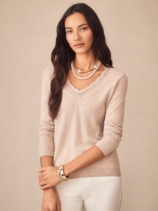 Woman wearing an oatmeal Evelyn Cashmere Sweater by J.McLaughlin, styled with layered pearl necklaces and bracelets, showcasing effortlessly stylish, enduring designs and a legacy of timeless fashion.