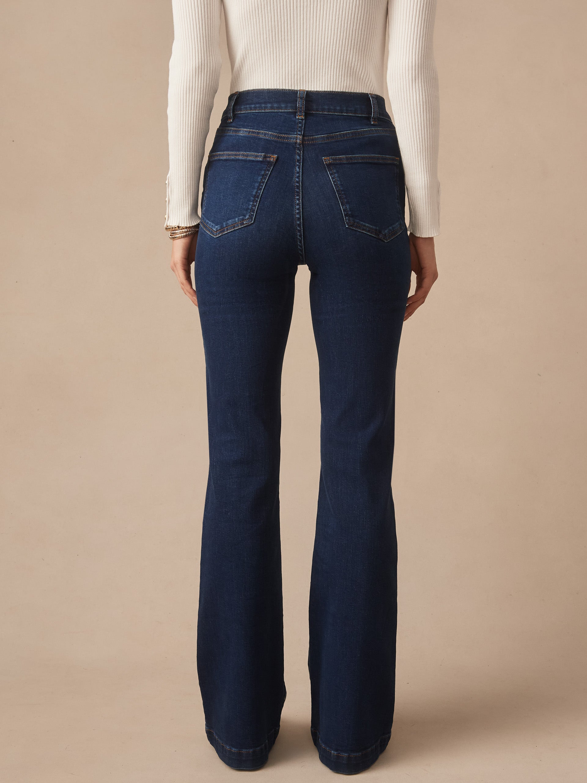 Back view of a woman wearing Domino Jeans by J.McLaughlin in dark denim, paired with a white ribbed long sleeve top, showcasing effortlessly stylish, enduring designs and a legacy of timeless fashion. A destination for defining style. Life, Well-Lived.