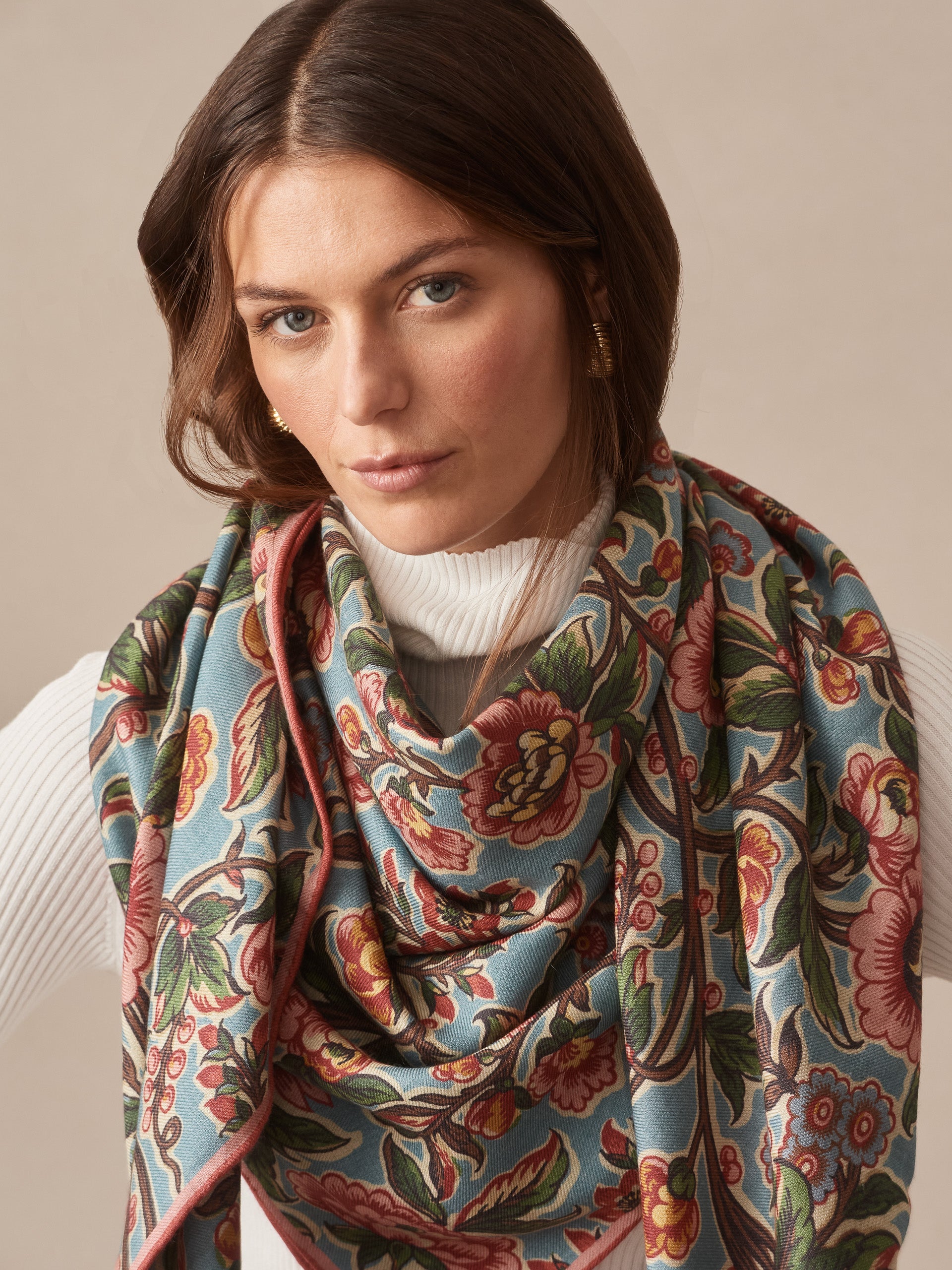 Woman wearing a Vanessa Scarf in Bucolic Blooms Border by J.McLaughlin, featuring vibrant floral patterns on a blue background, showcasing effortless style and enduring design.