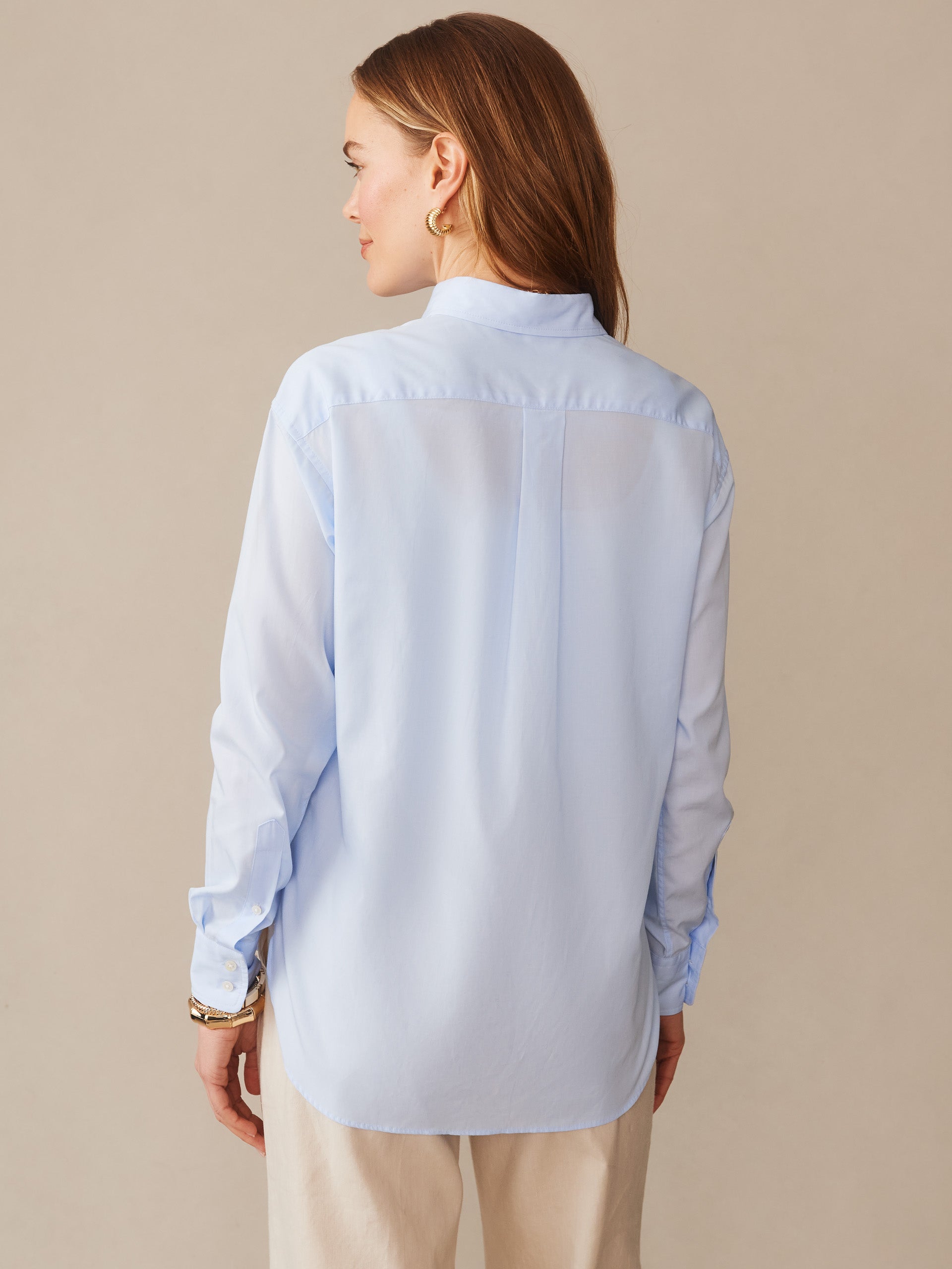 A woman wearing a light blue Finn Shirt by J.McLaughlin, showcasing effortlessly stylish, enduring designs crafted with innovative fabrics, embodying a legacy of timeless fashion.