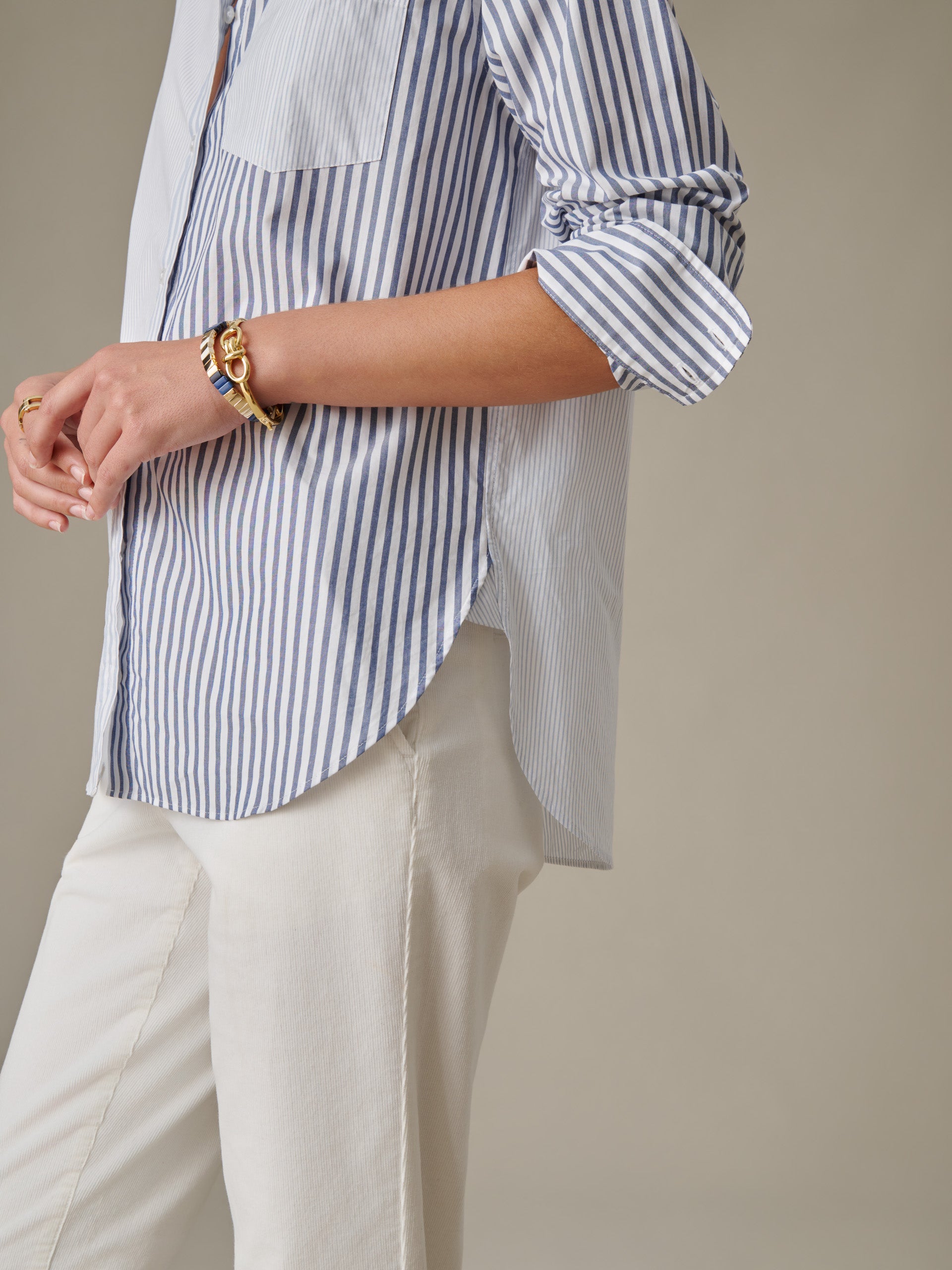 Close-up of a person wearing J.McLaughlin Finn Shirt in Stripe with rolled-up sleeves, paired with white pants and gold bracelets, showcasing timeless style and craftsmanship.