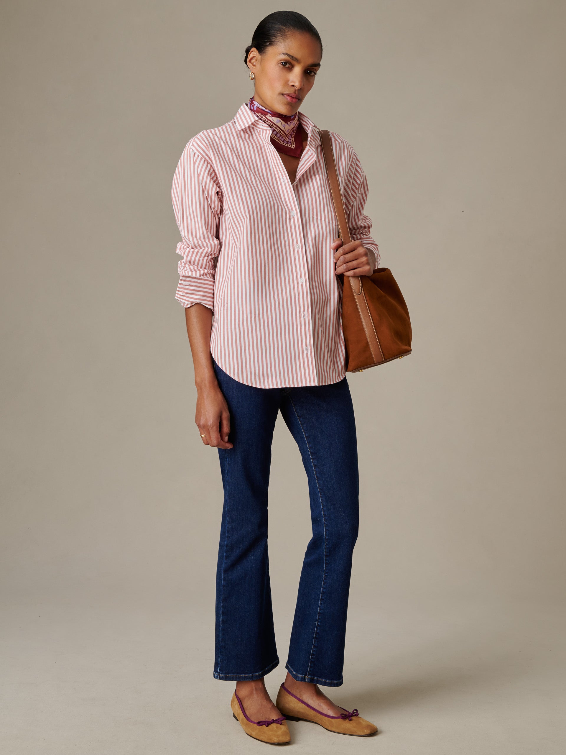 Woman wearing a Finn Shirt in Stripe by J.McLaughlin paired with dark blue jeans, a brown leather bag, and tan flats, showcasing timeless style and enduring design.
