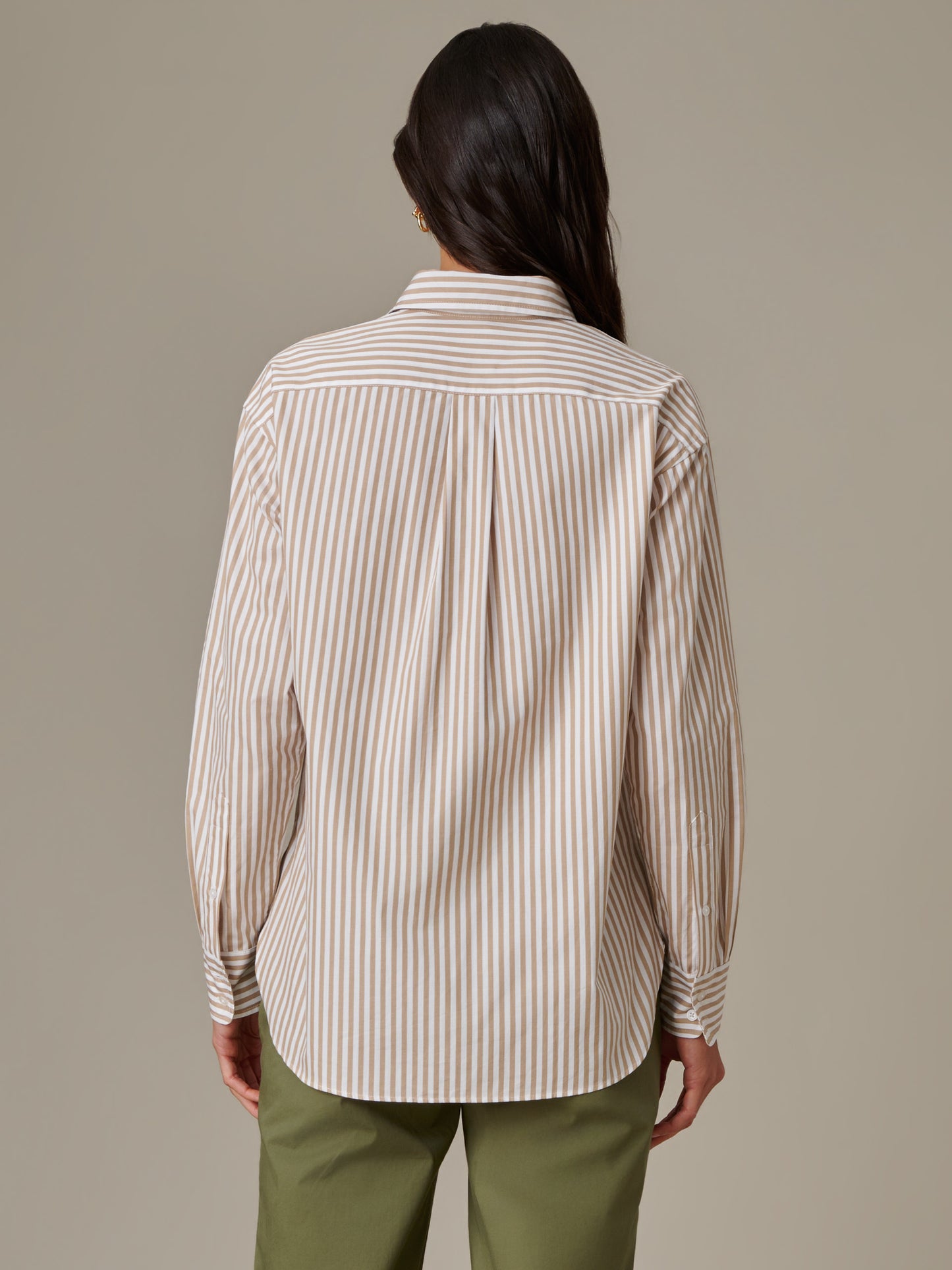Woman wearing a Finn Shirt in Stripe by J.McLaughlin, showcasing timeless style with beige and white vertical stripes paired with olive green pants in a classic, enduring design.