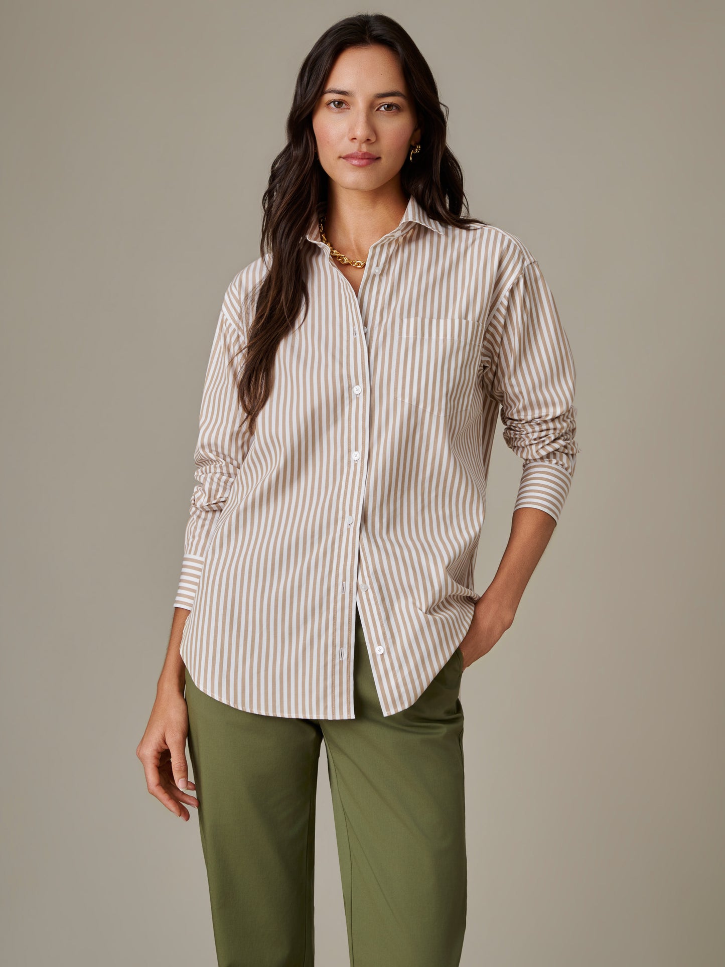 Woman wearing a J.McLaughlin Finn Shirt in Stripe, featuring beige and white vertical stripes, paired with olive green pants, embodying effortlessly stylish, enduring designs.