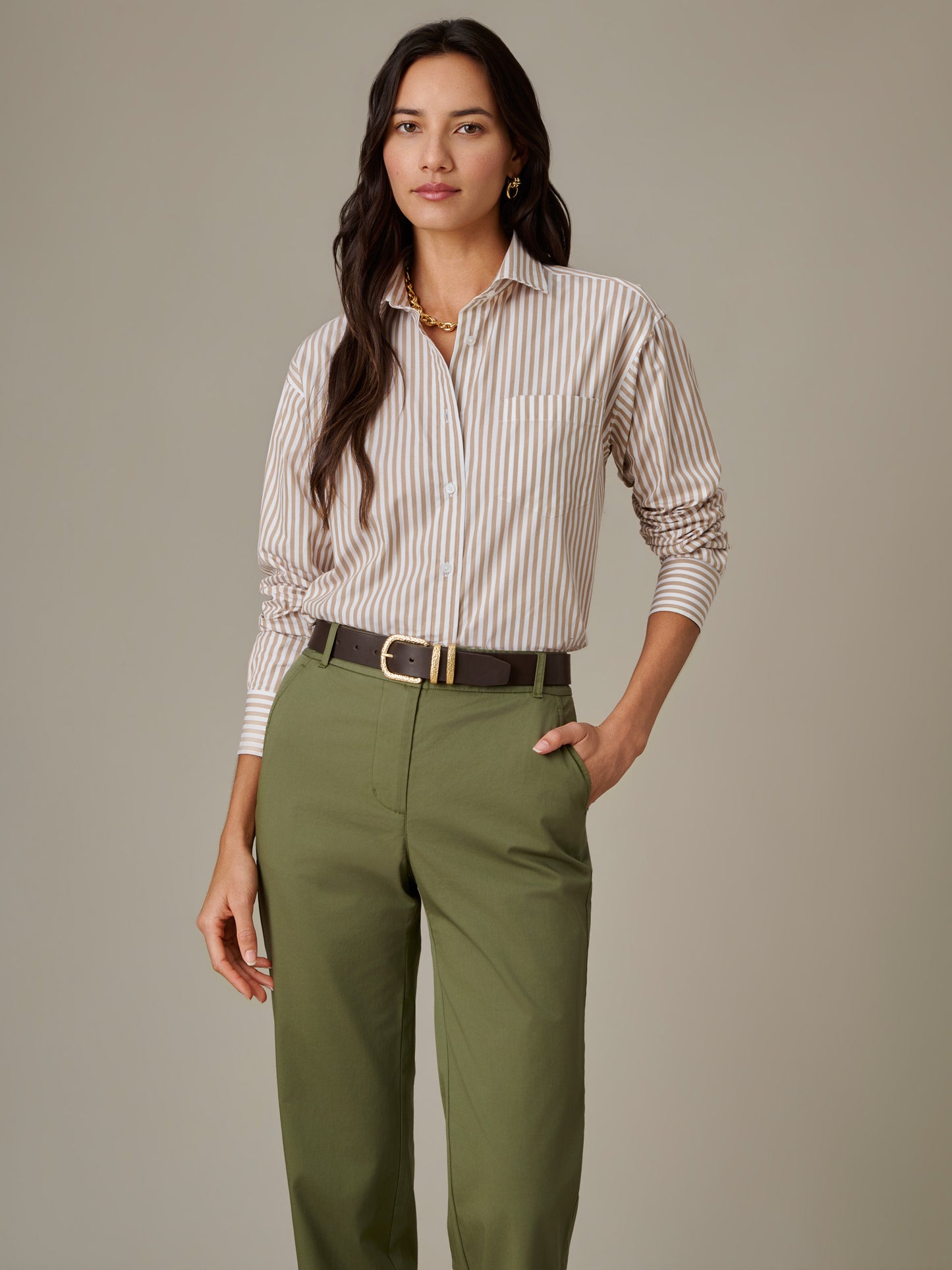 Woman modeling the Finn Shirt in Stripe by J.McLaughlin, paired with olive green pants and a dark belt, showcasing effortlessly stylish and enduring designs.