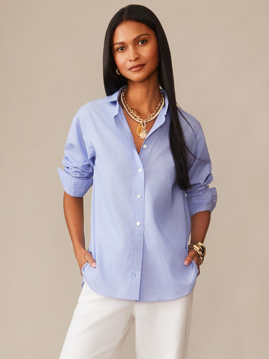 A woman wearing a light blue Finn Shirt by J.McLaughlin paired with white pants and gold jewelry, showcasing effortlessly stylish, enduring designs in a classic, timeless look.