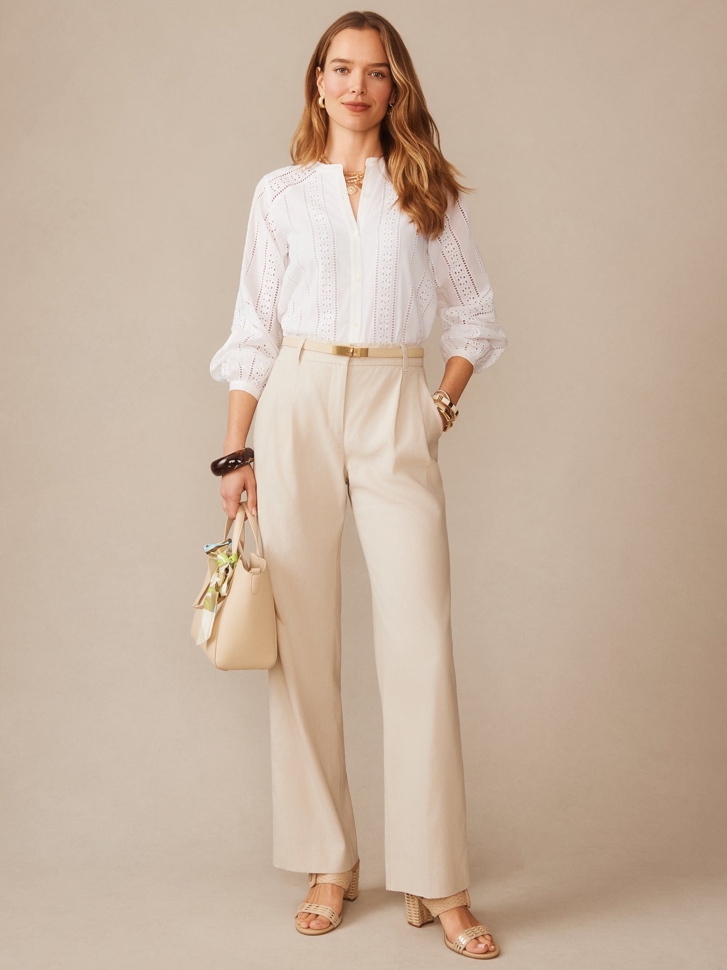A stylish woman wearing J.McLaughlin Fiona Linen Blend Pants in a stone color paired with a white blouse, accessorized elegantly, showcasing effortlessly stylish, enduring designs and innovative fabrics.