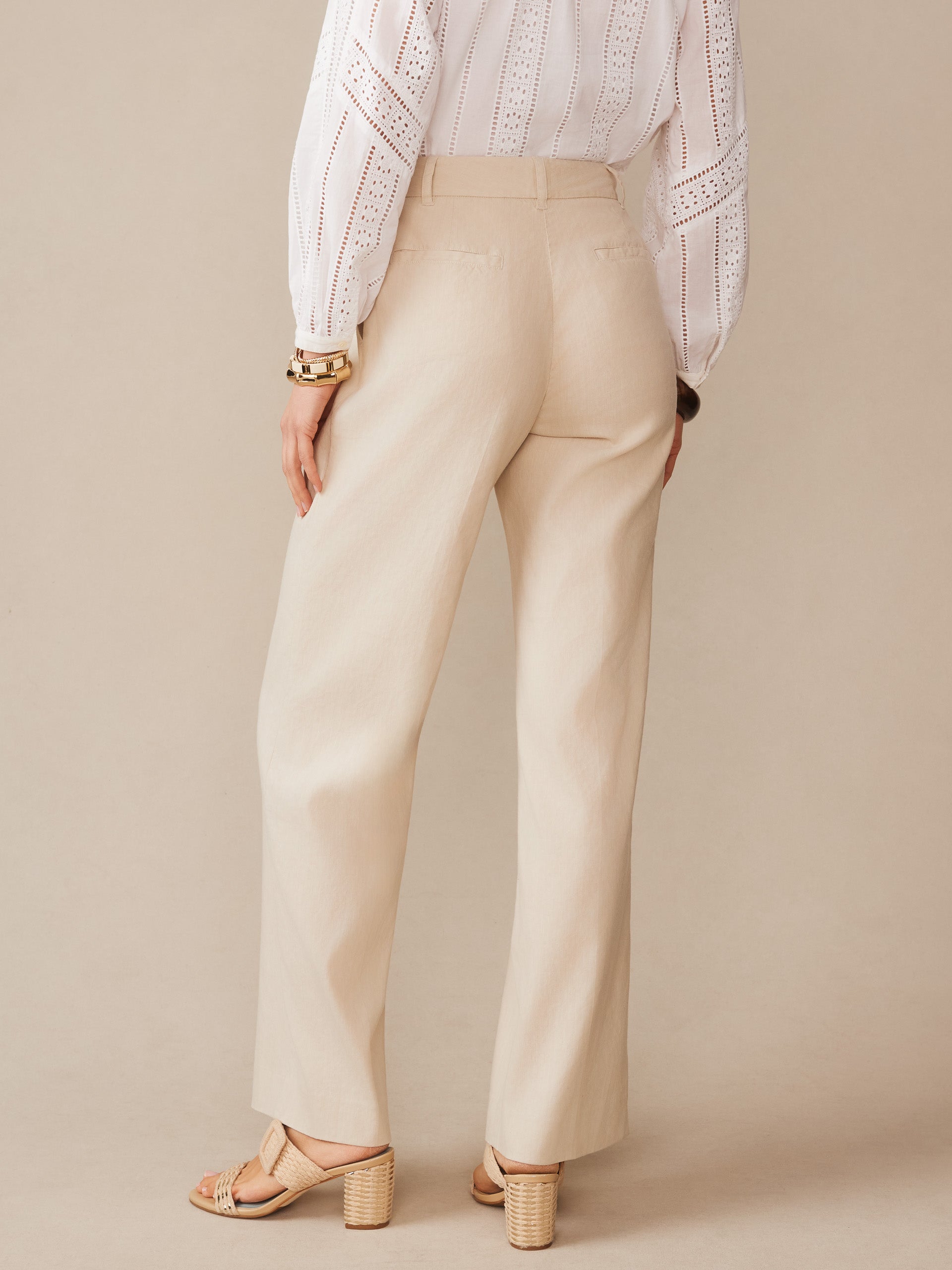 Woman wearing Fiona Linen Blend Pants by J.McLaughlin in a neutral stone color, paired with a white eyelet blouse and heeled sandals, showcasing effortlessly stylish, enduring designs and innovative fabrics.