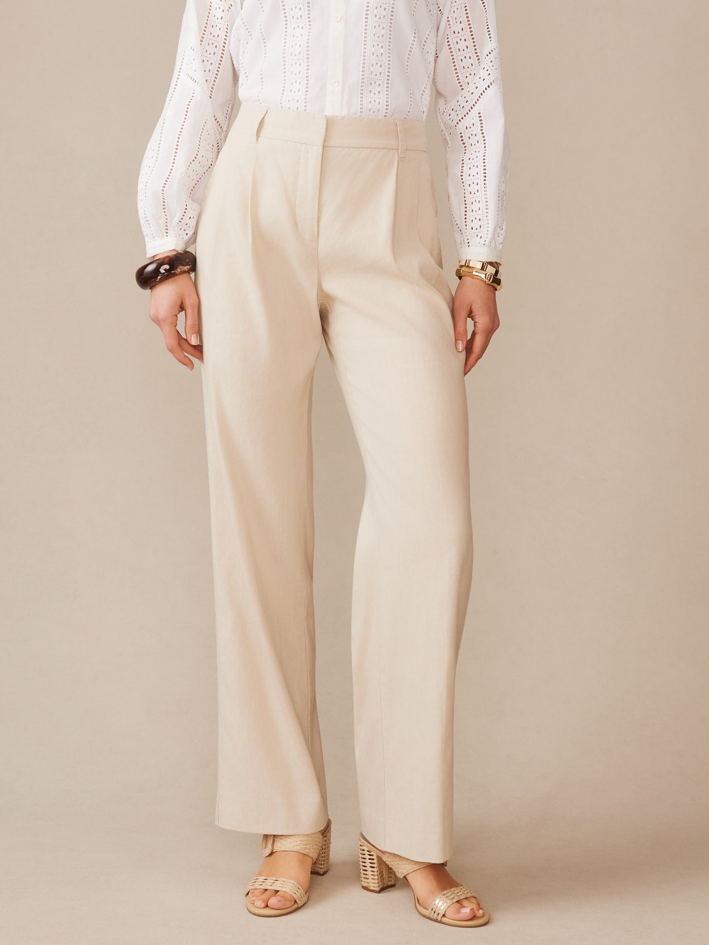 A model wearing Fiona Linen Blend Pants by J.McLaughlin in a light stone color paired with a white eyelet blouse and beige woven sandals, showcasing effortlessly stylish, enduring designs in innovative fabrics for a timeless fashion legacy.
