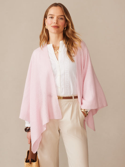 Woman wearing a soft pink Julianne Cashmere Wrap over a white blouse and beige pants, styled with gold accessories and a woven handbag, embodying effortlessly stylish, enduring designs by J.McLaughlin.